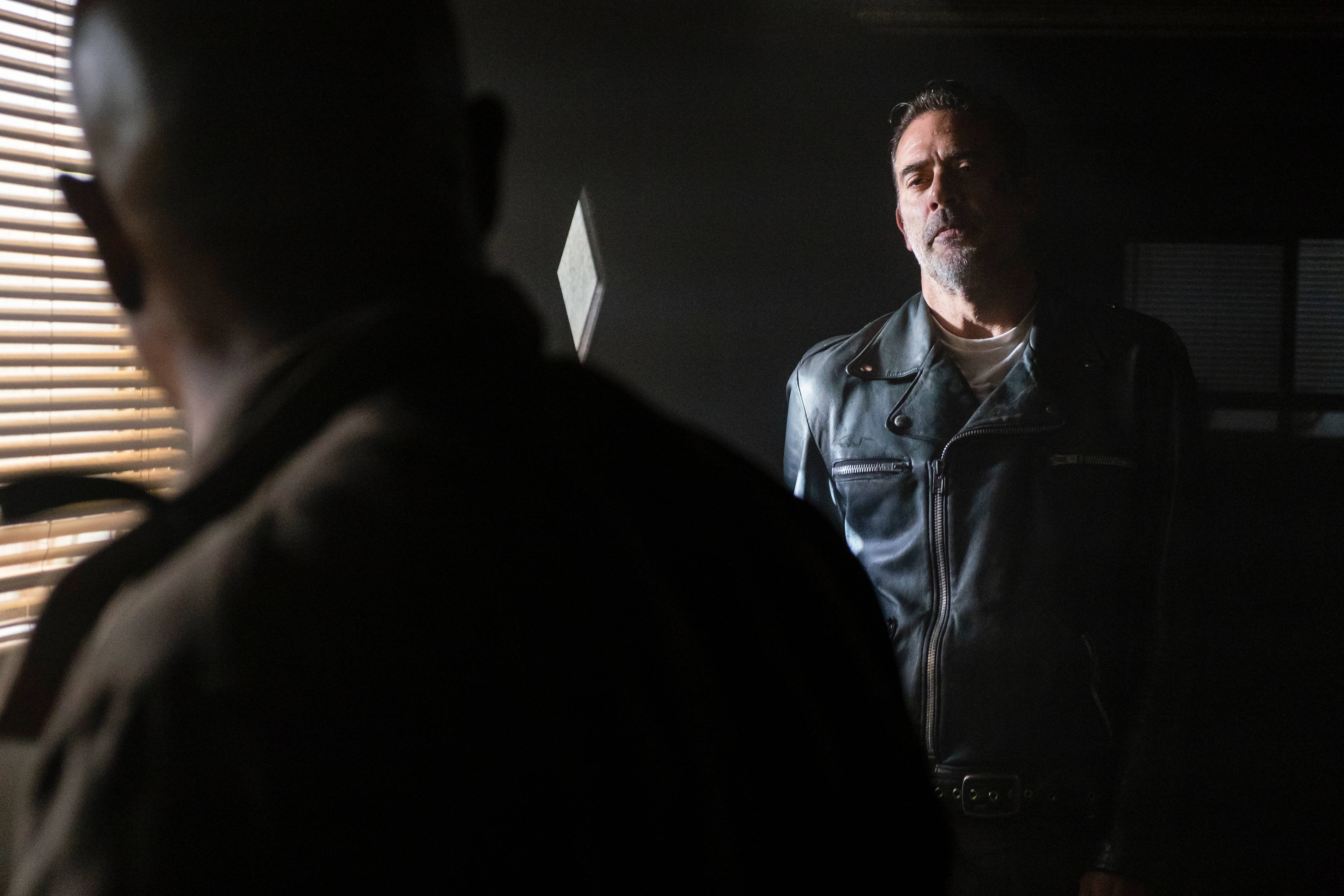 Negan 桌布 壁紙 — 一個穿皮夾克的男人站在昏暗燈光下，面向百葉窗附近另一個剪影人物。