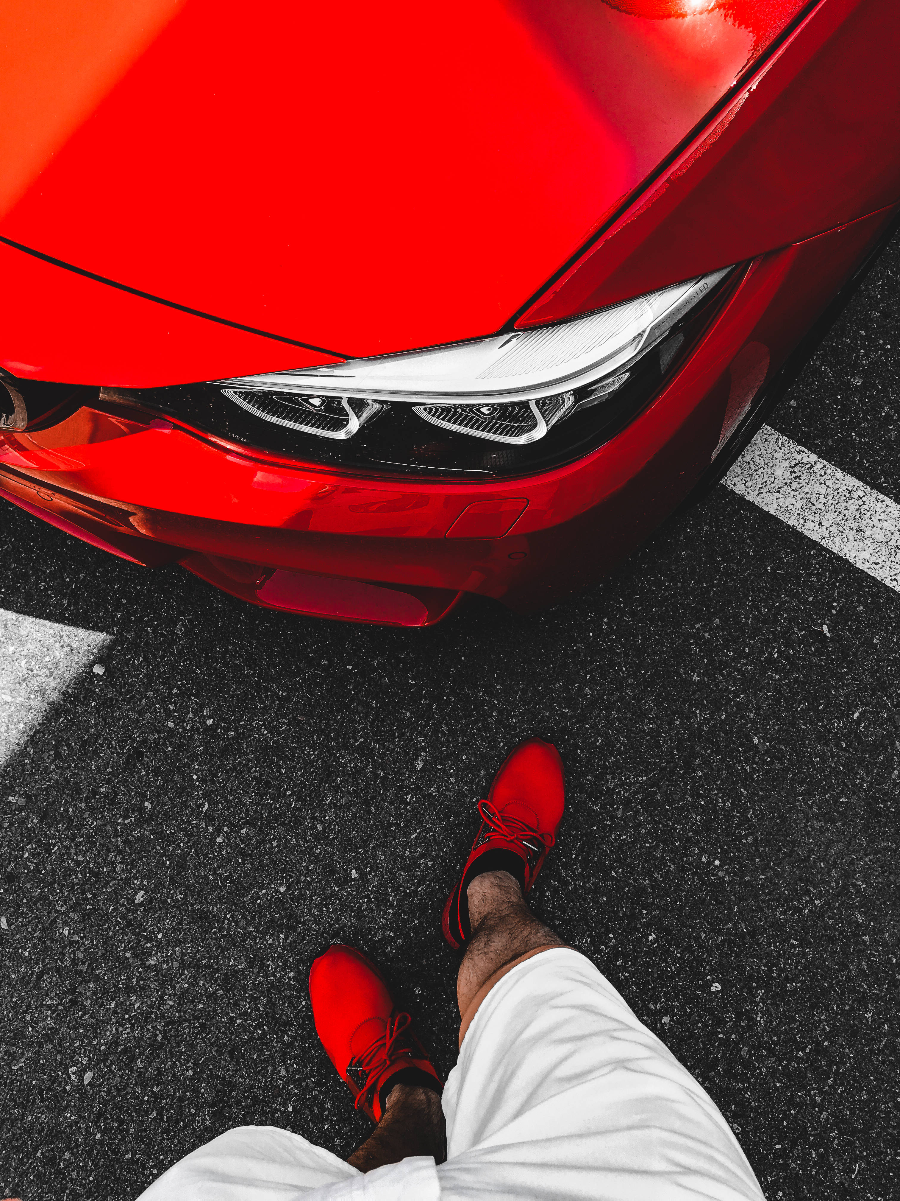 iPhone 8 red 桌布 壁紙 — 一個穿紅鞋的人站在有白色停車線的瀝青路上，旁邊是一輛亮紅色汽車。