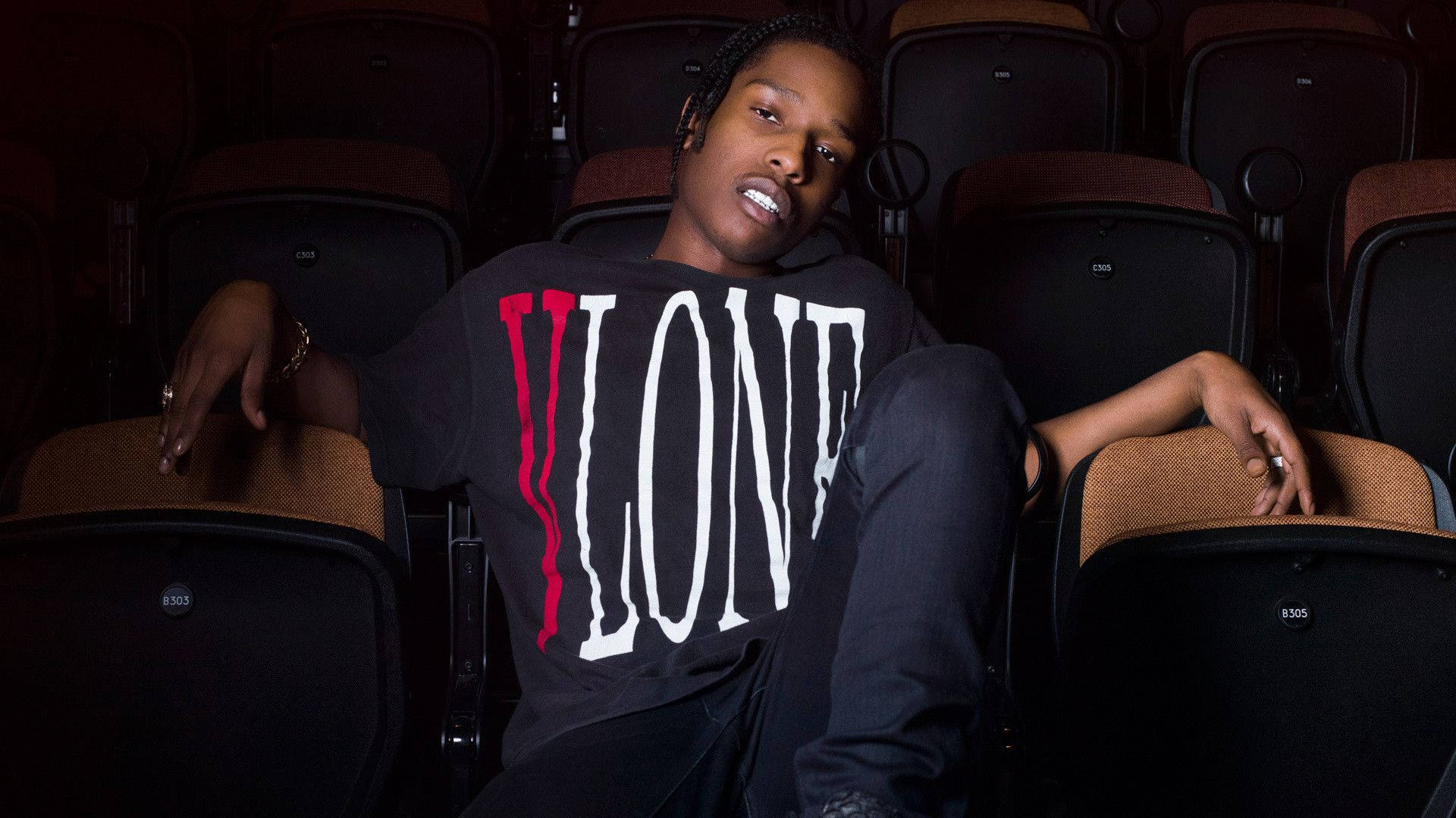 Vlone 桌布 壁紙 — 一個穿著「LONE」T恤的年輕人自信地躺在昏暗的戲院座位上，散發出酷炫的都市氣息。