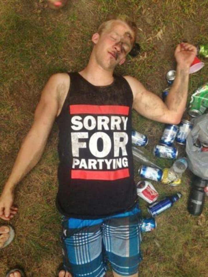 搞笑 桌布 壁紙 — 一個穿著「Sorry For Partying」背心的年輕男子躺在草地上睡著了，周圍散落著空啤酒罐和杯子。