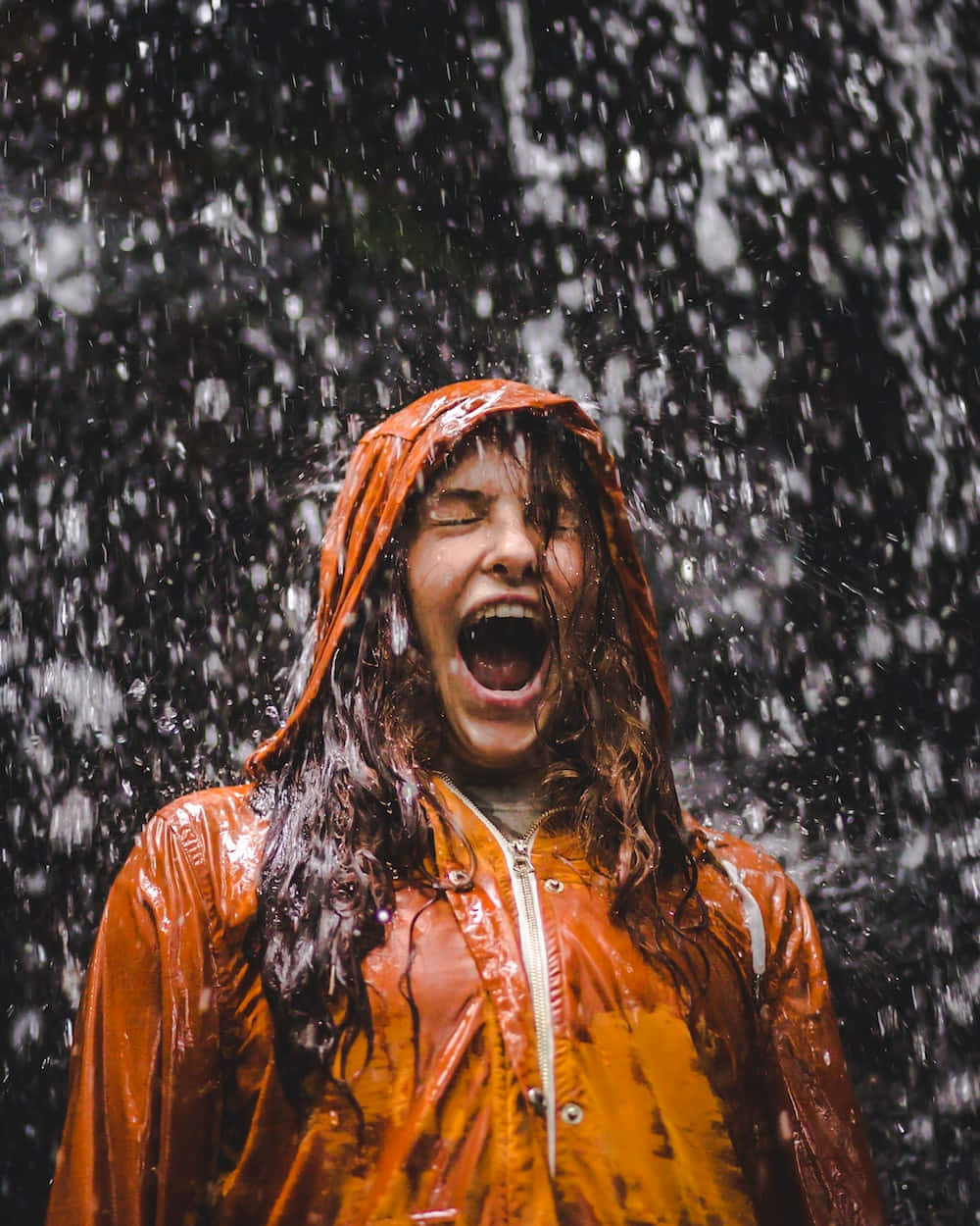下雨 桌布 壁紙 — 一個穿著亮橙色雨衣的人在大雨中開心大笑，雙眼緊閉，嘴巴大開。