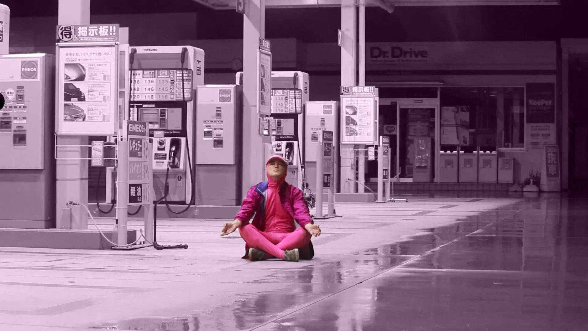 joji 桌布 壁紙 — 一個穿著亮粉紅色的人晚上盤腿坐在潮濕的加油站地板上，周圍是紫色燈光下的油泵。