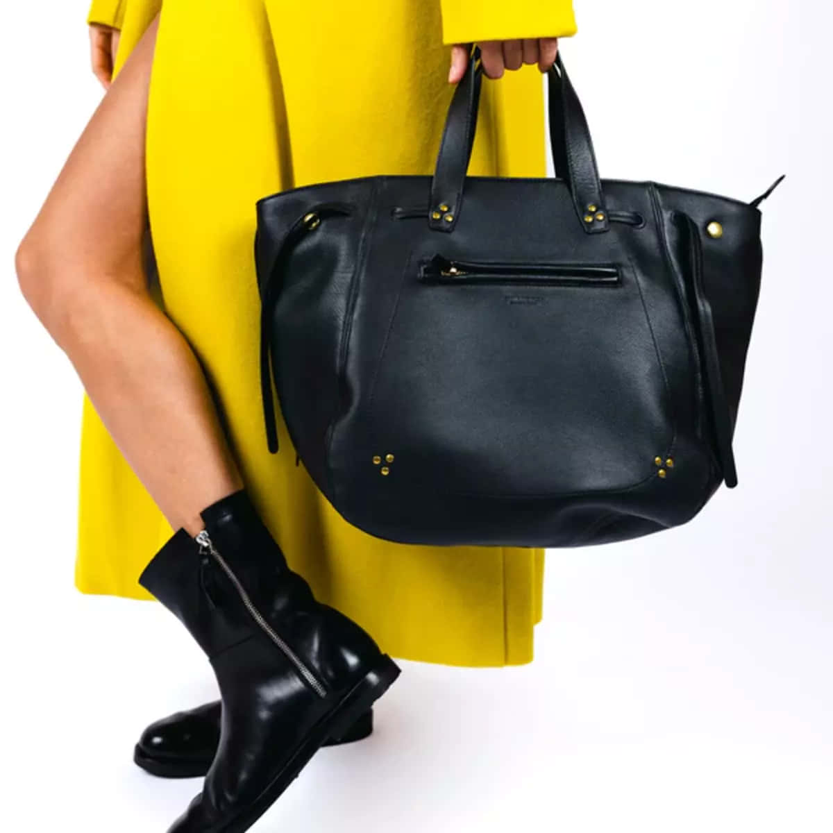 Handbag 桌布 壁紙 — 一個穿著亮黃色外套的人，在白色背景前拿著一個帶有金色裝飾的黑色皮革托特包。