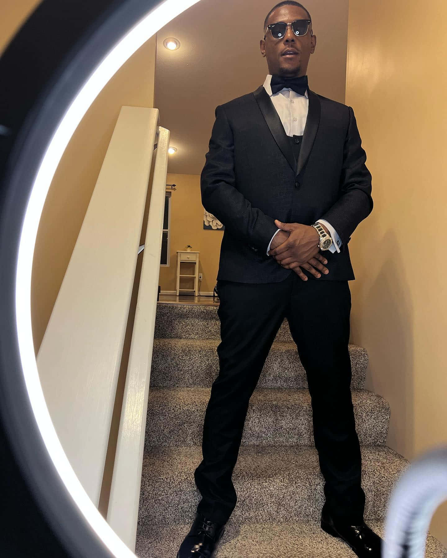 Man In Suit 桌布 壁紙 — 一個穿著俐落黑色燕尾服和太陽眼鏡的男人自信地站在鋪有地毯的樓梯上，周圍環繞著發光的環形燈。