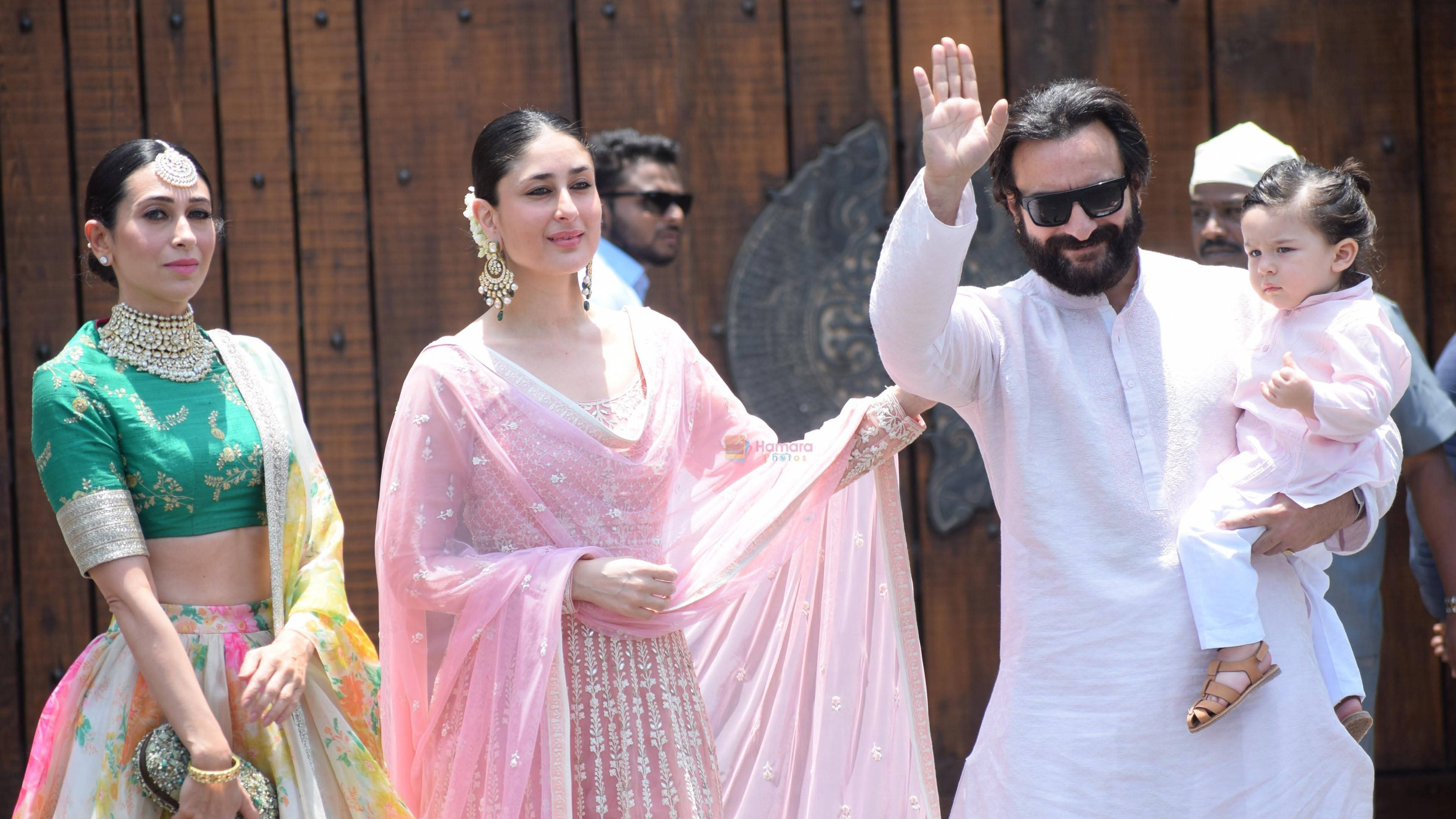 Saif Ali Khan 桌布 壁紙 — 一個穿著傳統印度服飾的家庭在明亮的日光下，以木製背景為襯，向人群揮手。