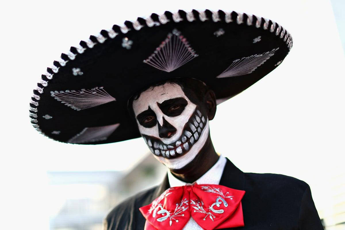 Dia De Los Muertos 桌布 壁紙 — 一個穿著傳統墨西哥亡靈節服飾的人，帶有骷髏妝容和一頂大型黑色闊邊帽。