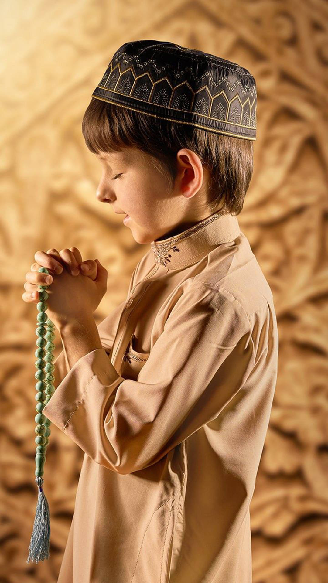 Praying 桌布 壁紙 — 一個穿著傳統服飾的男孩，手持綠色念珠，在金色華麗的牆前祈禱。