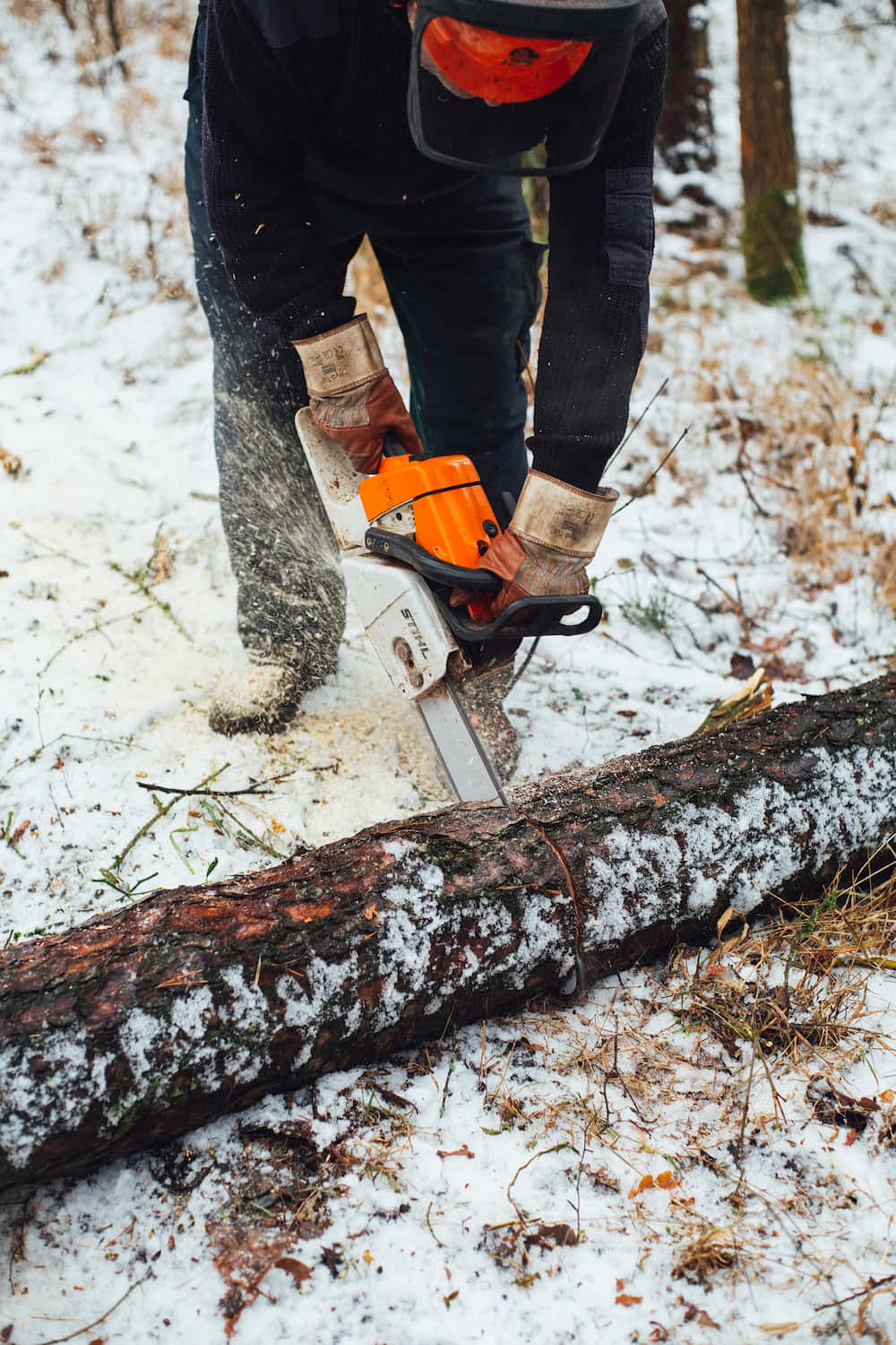 工具 桌布 壁紙 — 一個穿著冬季裝備的人在雪地森林中用橙色電鋸鋸開一條鋪滿雪的木頭。