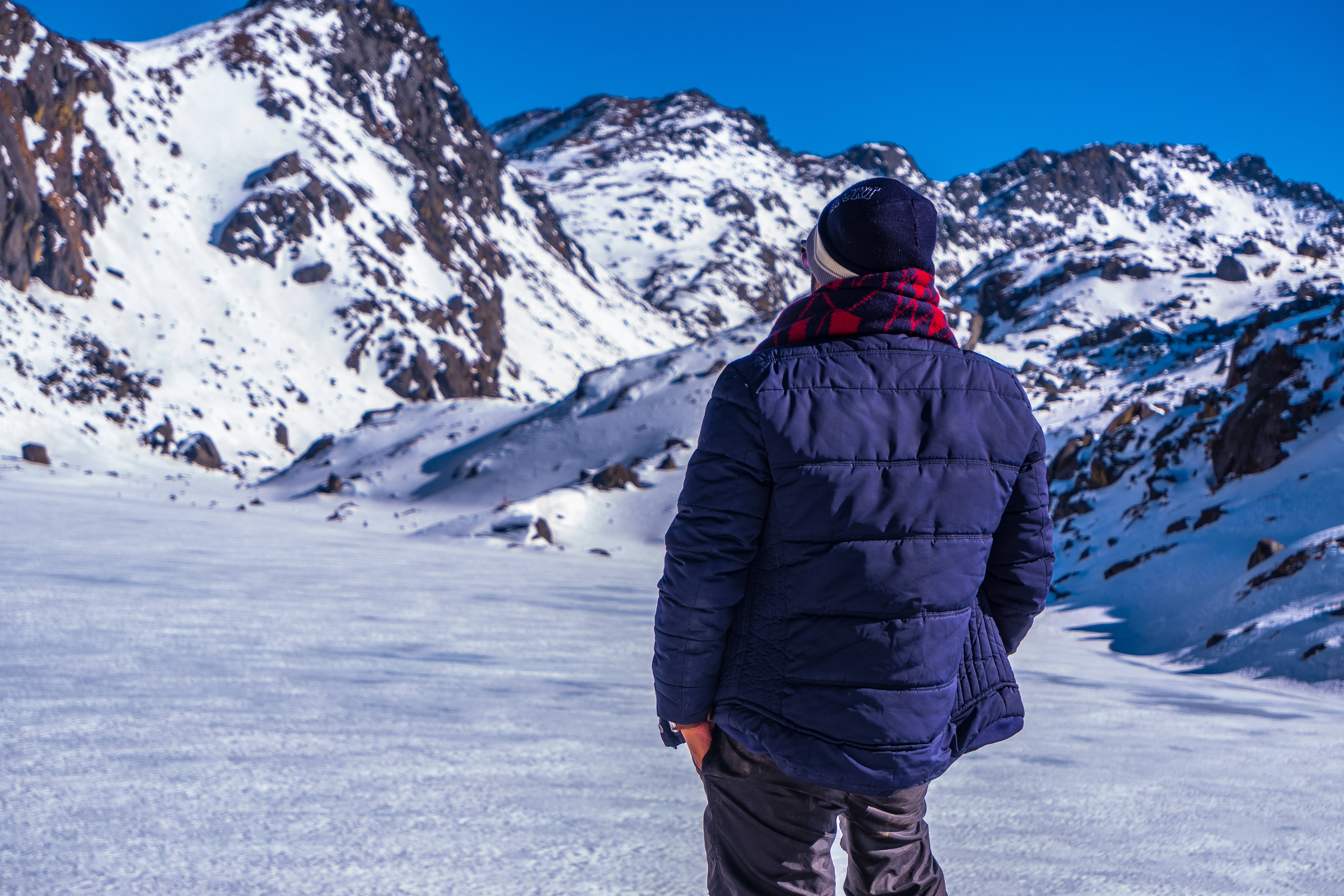 Nepal 桌布 壁紙 — 一個穿著冬季裝備的人獨自站在白雪覆蓋的山原上，凝視著晴朗藍天下崎嶇的雪峰。