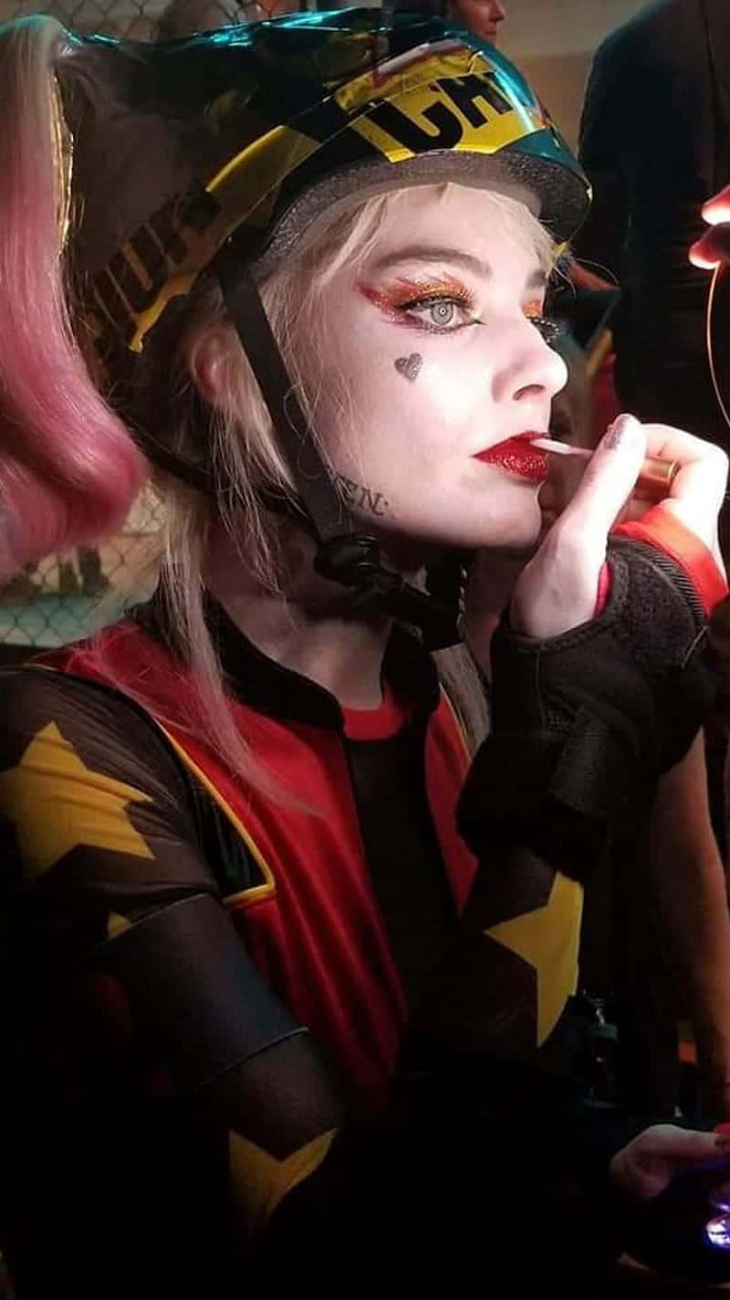 Margot Robbie Harley Quinn 桌布 壁紙 — 一個穿著哈莉·奎茵服裝的人正在塗紅色口紅，戴著裝飾頭盔和星星圖案服裝。