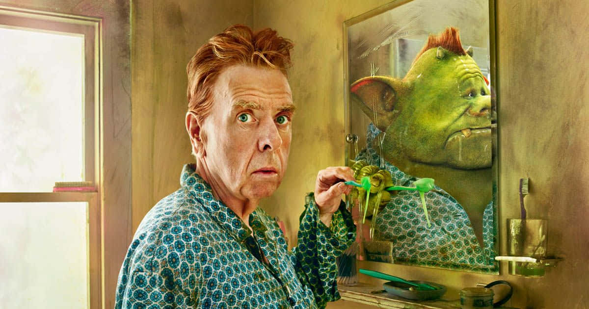 Timothy Spall 桌布 壁紙 — 一個穿著圖案睡袍的男人在刷牙，同時盯著浴室鏡中自己怪異的綠色倒影。