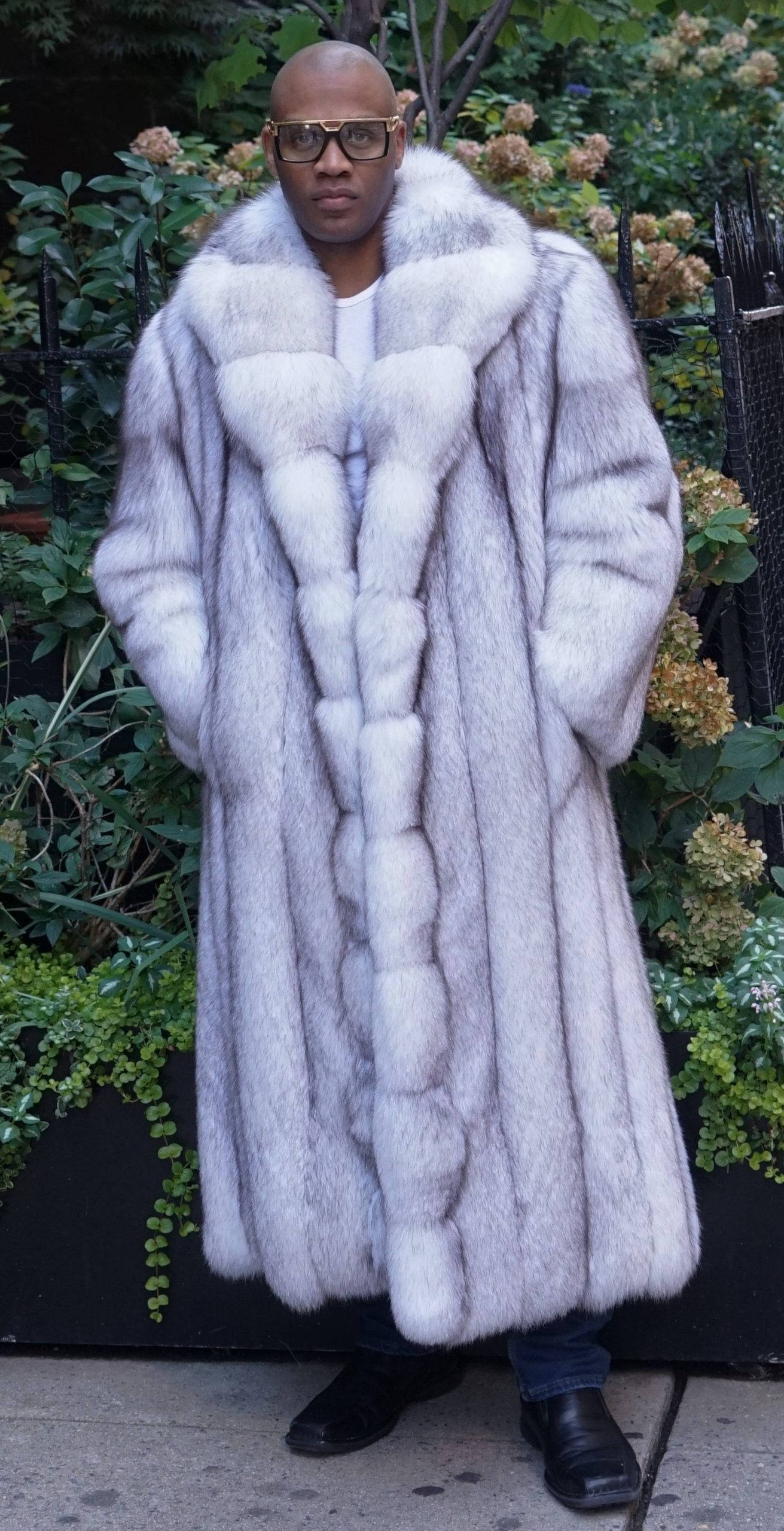 fur 桌布 壁紙 — 一個穿著寬大銀狐皮草大衣的男人自信地站在茂密的綠色花園背景下。