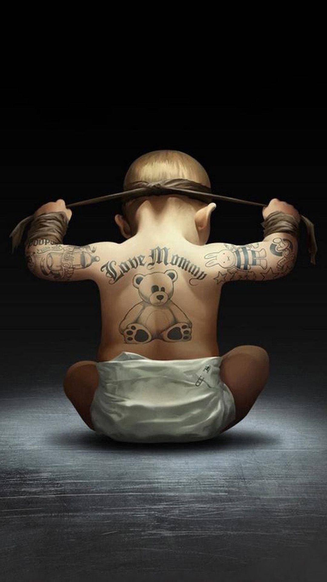 寶寶 桌布 壁紙 — 一個穿著尿布的嬰兒背對觀眾坐著，露出包括泰迪熊和「Love Mommy」在內的刺青，背景是深色地板。