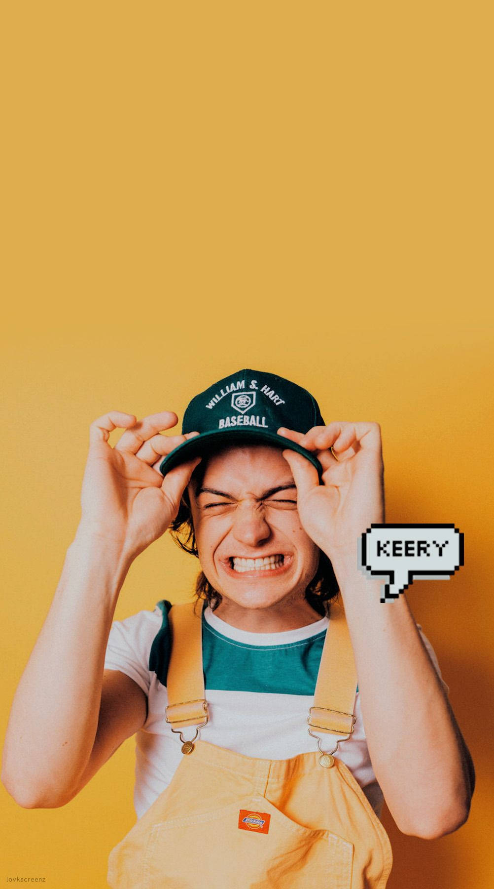 Joe Keery 桌布 壁紙 — 一個穿著工裝褲和棒球帽的人，在純黃色背景前做出兇狠的表情，旁邊有一個像素對話框寫著「KEERY」。