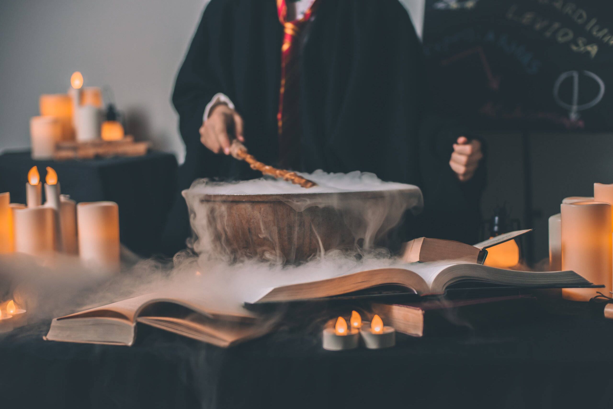 魔法動圖 桌布 壁紙 — 一個穿著巫師袍的人對一個冒著蒸氣的大鍋施法，周圍有發光的蠟燭和打開的咒語書。