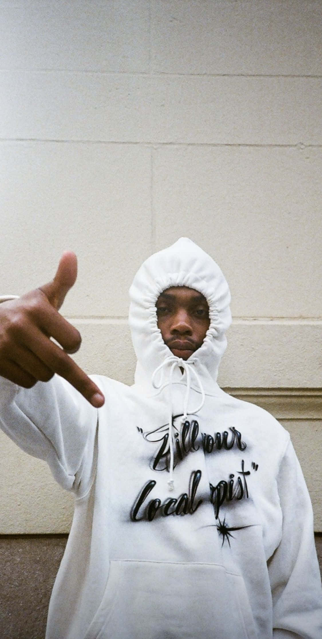 Rappers 桌布 壁紙 — 一個穿著帶有黑色文字的白色連帽衫的人，在純米色牆前面直接指向相機。