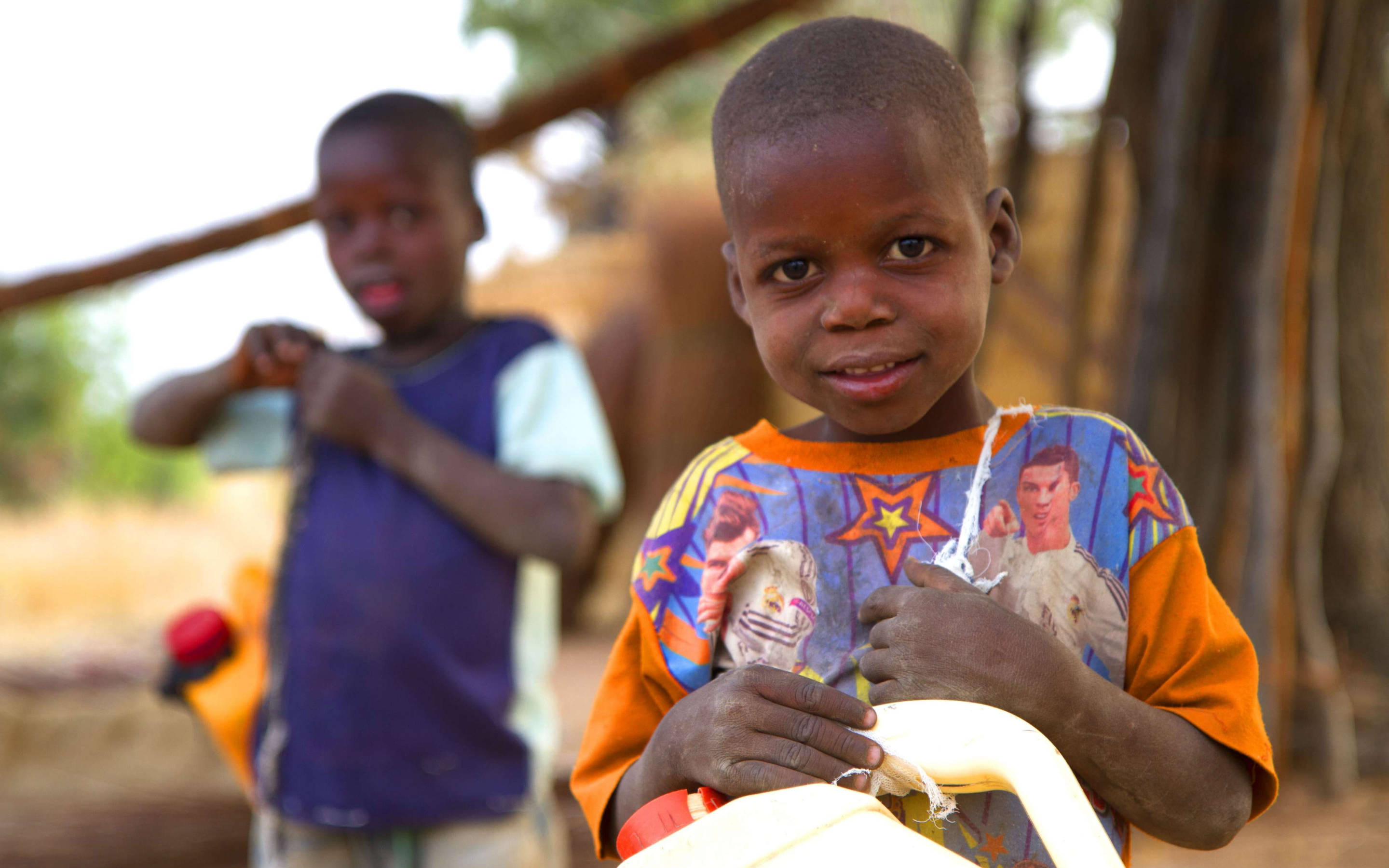 Nigeria 桌布 壁紙 — 一個穿著彩色襯衫的小男孩拿著水壺，溫柔地微笑看著鏡頭。