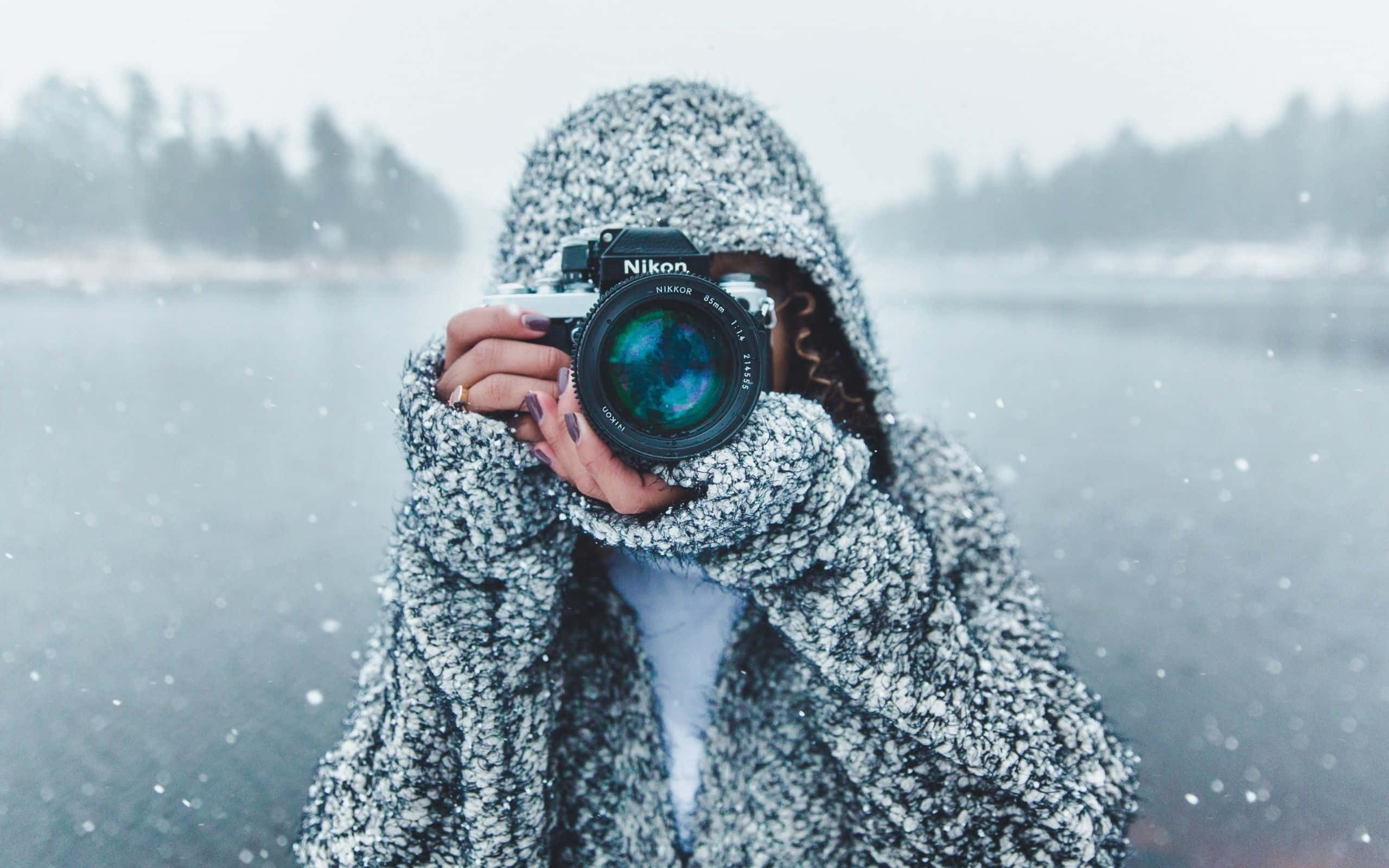 攝影 桌布 壁紙 — 一個穿著有紋理連帽外套的人，在雪霧瀰漫的湖邊背景下，將相機舉到臉前。