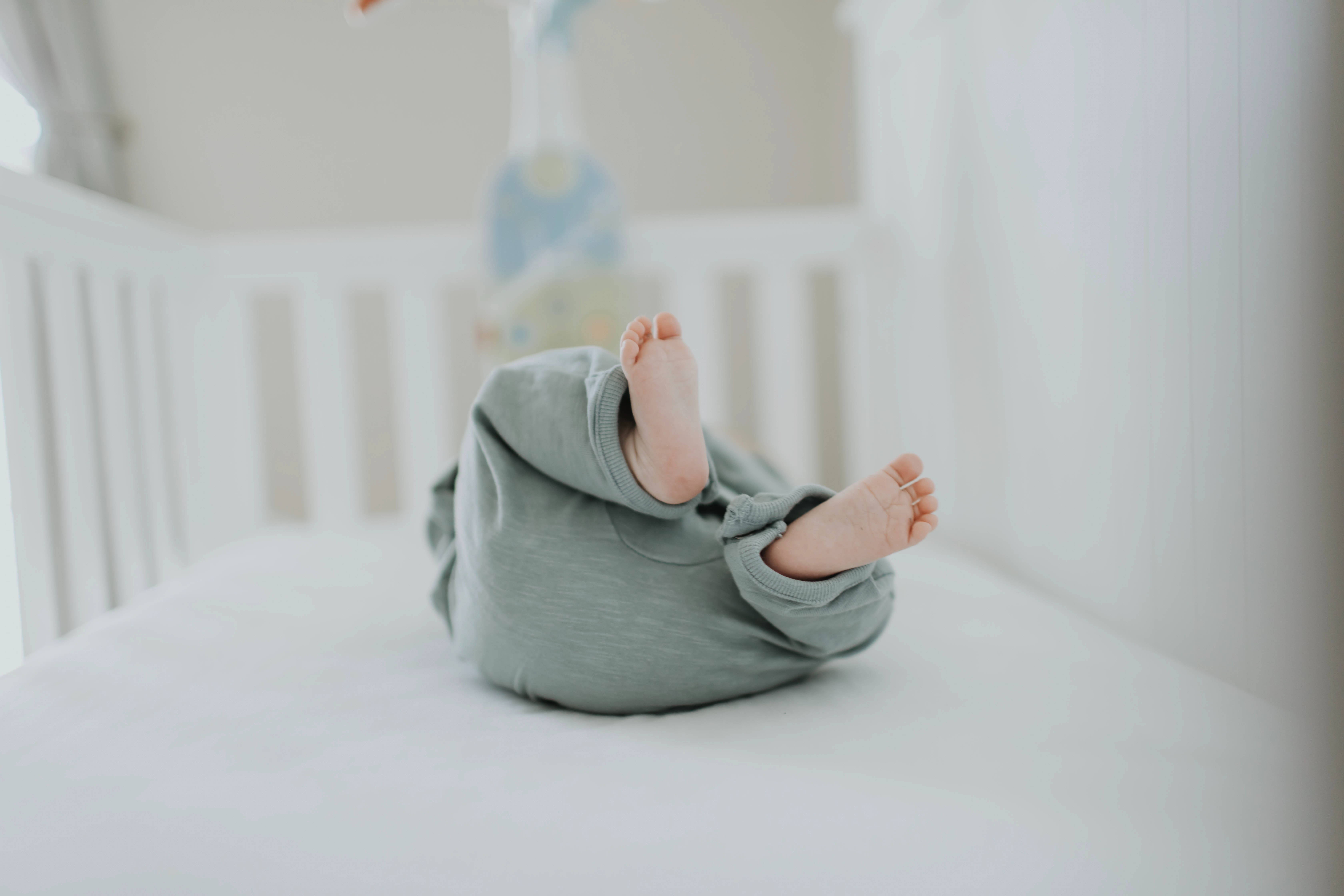 Baby HD 桌布 壁紙 — 一個穿著柔軟綠色睡衣的嬰兒盤腿坐在白色嬰兒床裡，赤腳在明亮通風的背景下清晰可見。
