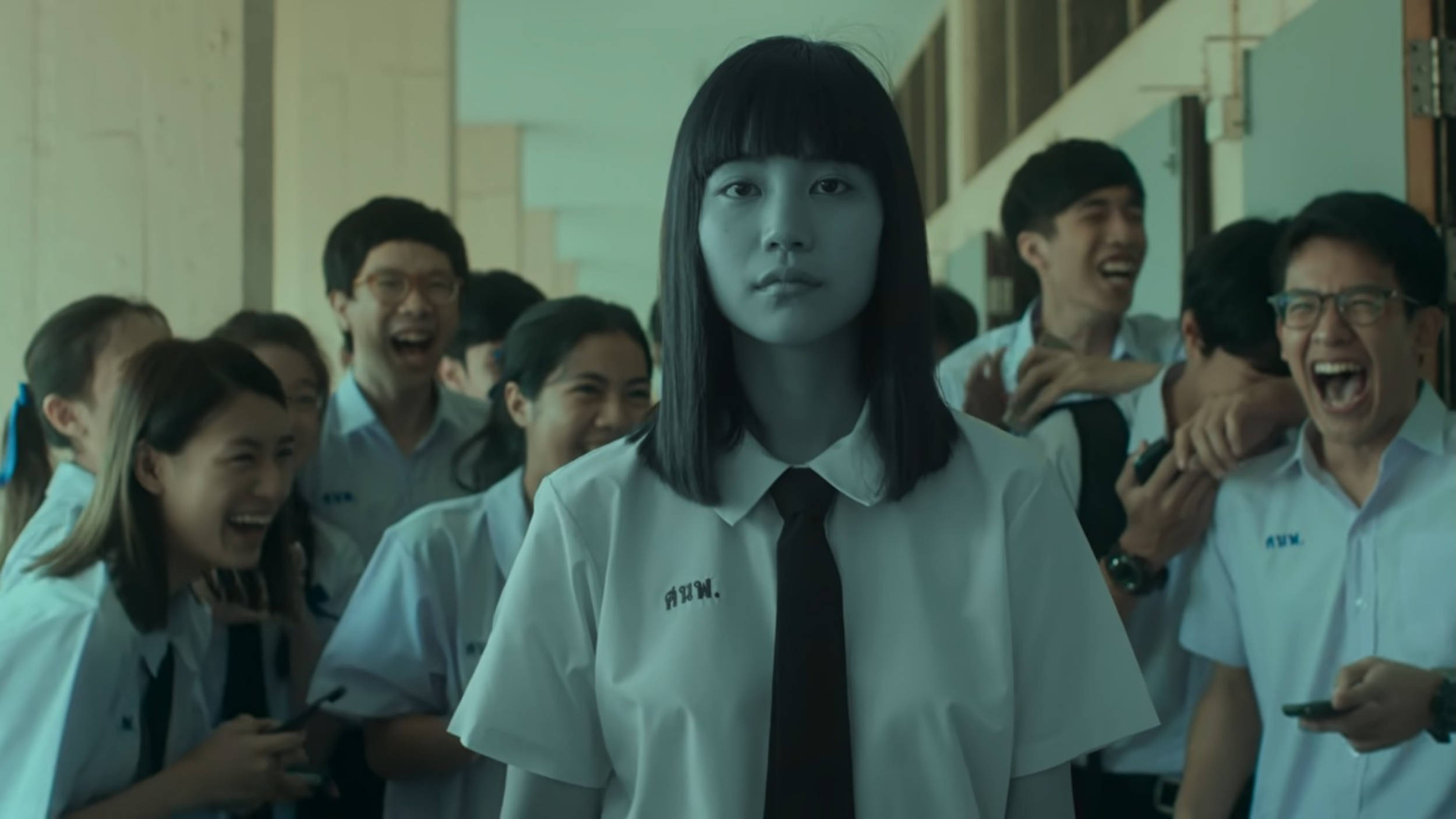 恐怖 桌布 壁紙 — 一個穿著校服的嚴肅女學生站在畫面中央，而同學們在她身後的走廊上大笑和歡呼。