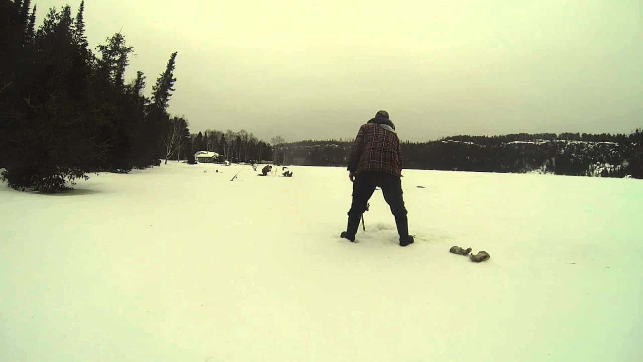 Ice Fishing 桌布 壁紙 — 一個穿著格子外套的孤獨人走過廣闊的雪地，有常青樹和遠方的山丘，天空多雲。