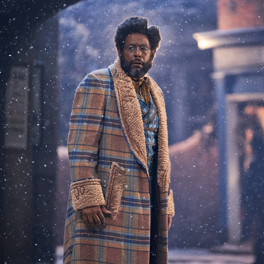 Celebrity 桌布 壁紙 — 一個穿著格紋羊毛外套的男人站在積雪的城市小巷中，雪花在他周圍飄落。