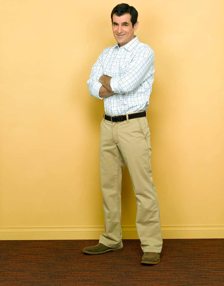 Ty Burrell 桌布 壁紙 — 一個穿著格紋襯衫和卡其褲的男人自信地交叉雙臂，靠著一面純黃色的牆。