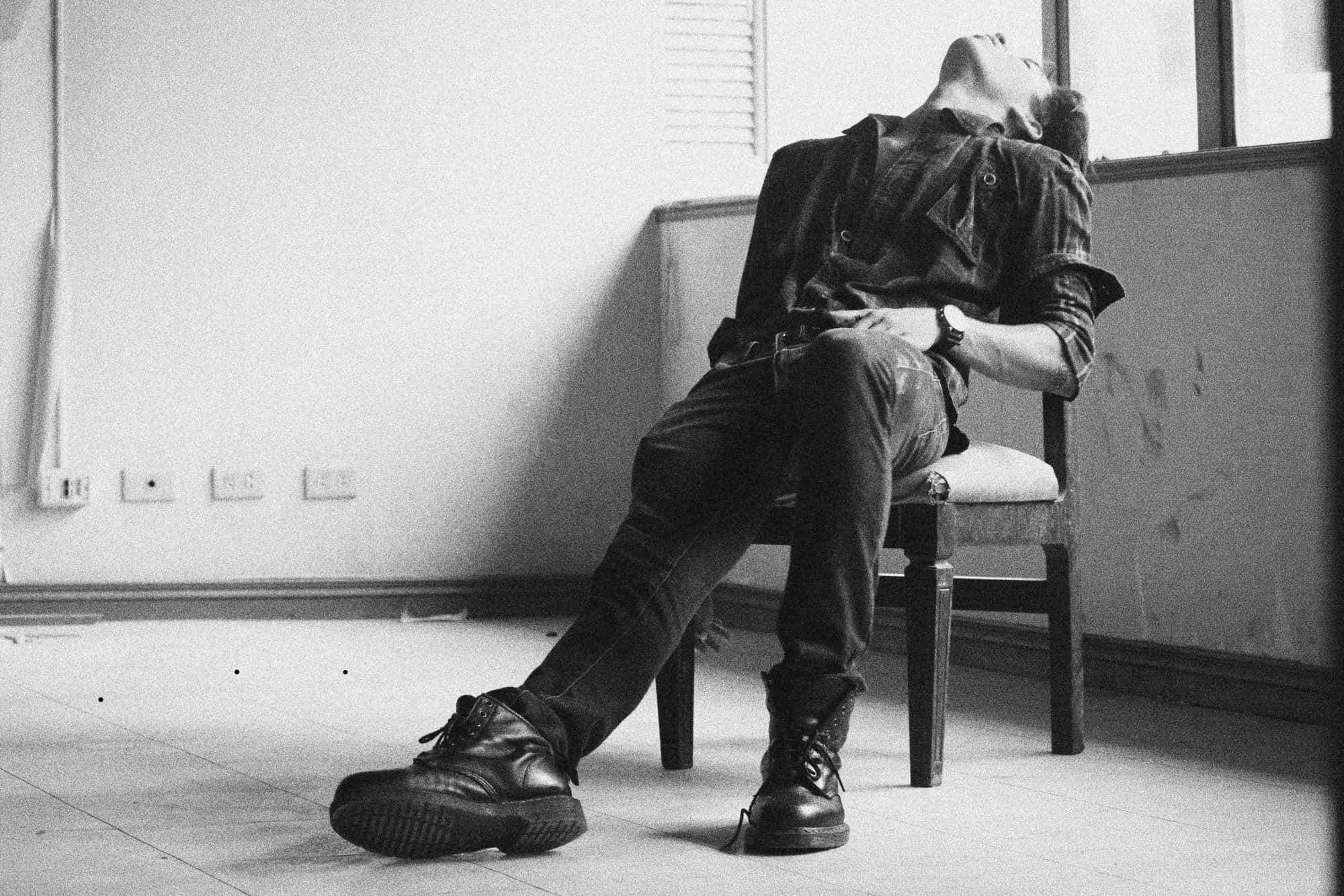 Alone 桌布 壁紙 — 一個穿著格紋襯衫和靴子的男人癱坐在椅子上，頭向後仰，身處一個光線強烈的空房間。
