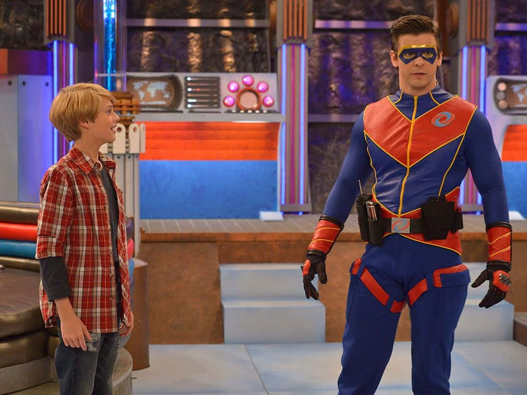 henry danger 桌布 壁紙 — 一個穿著格紋襯衫的小男孩站在一個未來實驗室內，旁邊是一位穿著藍色和紅色服裝的超級英雄。