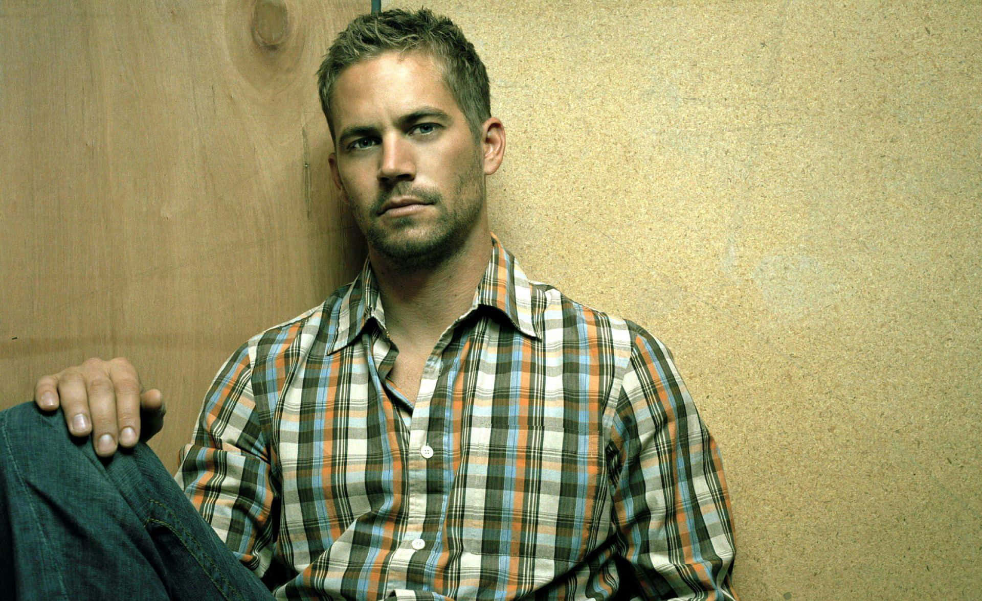 Paul Walker 桌布 壁紙 — 一個穿著格紋襯衫的男人，表情嚴肅地靠在木牆上。