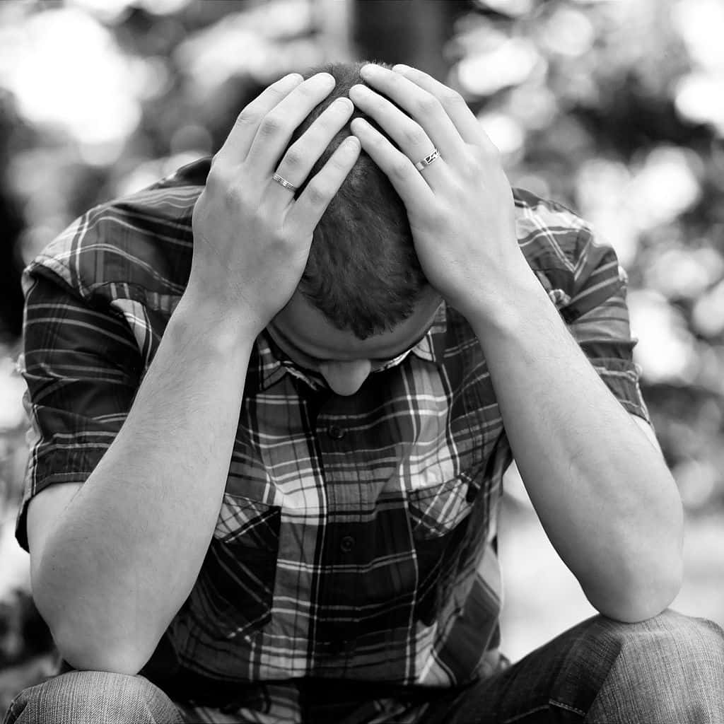 Depressed 桌布 壁紙 — 一個穿著格紋襯衫的男人坐著，雙手抱頭，手疊在額頭上，黑白照片。