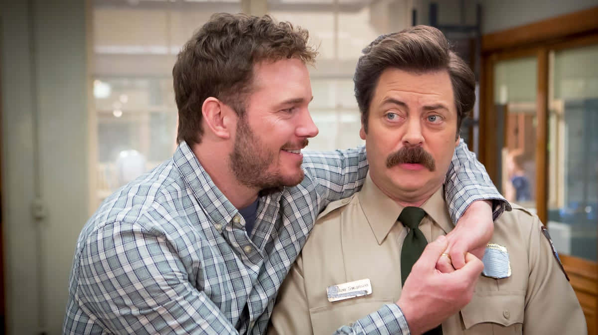 nick offerman 桌布 壁紙 — 一個穿著格紋襯衫的男人頑皮地摟住另一個穿著警察制服、面露驚訝的男人。