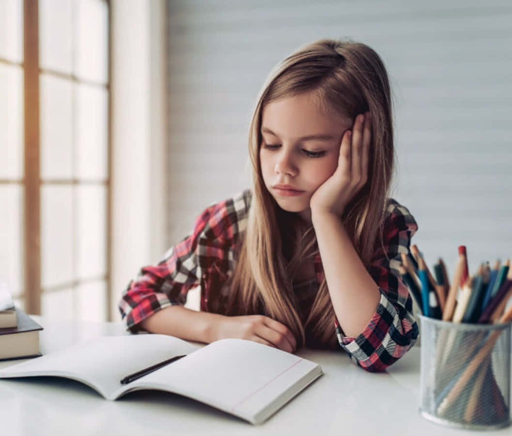Study Girl 桌布 壁紙 — 一個穿著格紋襯衫的疲倦女孩，在明亮的窗邊書桌讀書時將頭靠在手上。