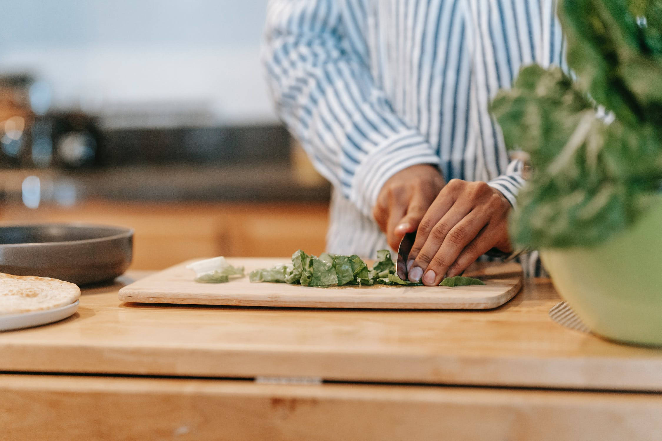 Healthy Food 桌布 壁紙 — 一個穿著條紋襯衫的人，在明亮的廚房裡，在木製砧板上切新鮮的綠色生菜。