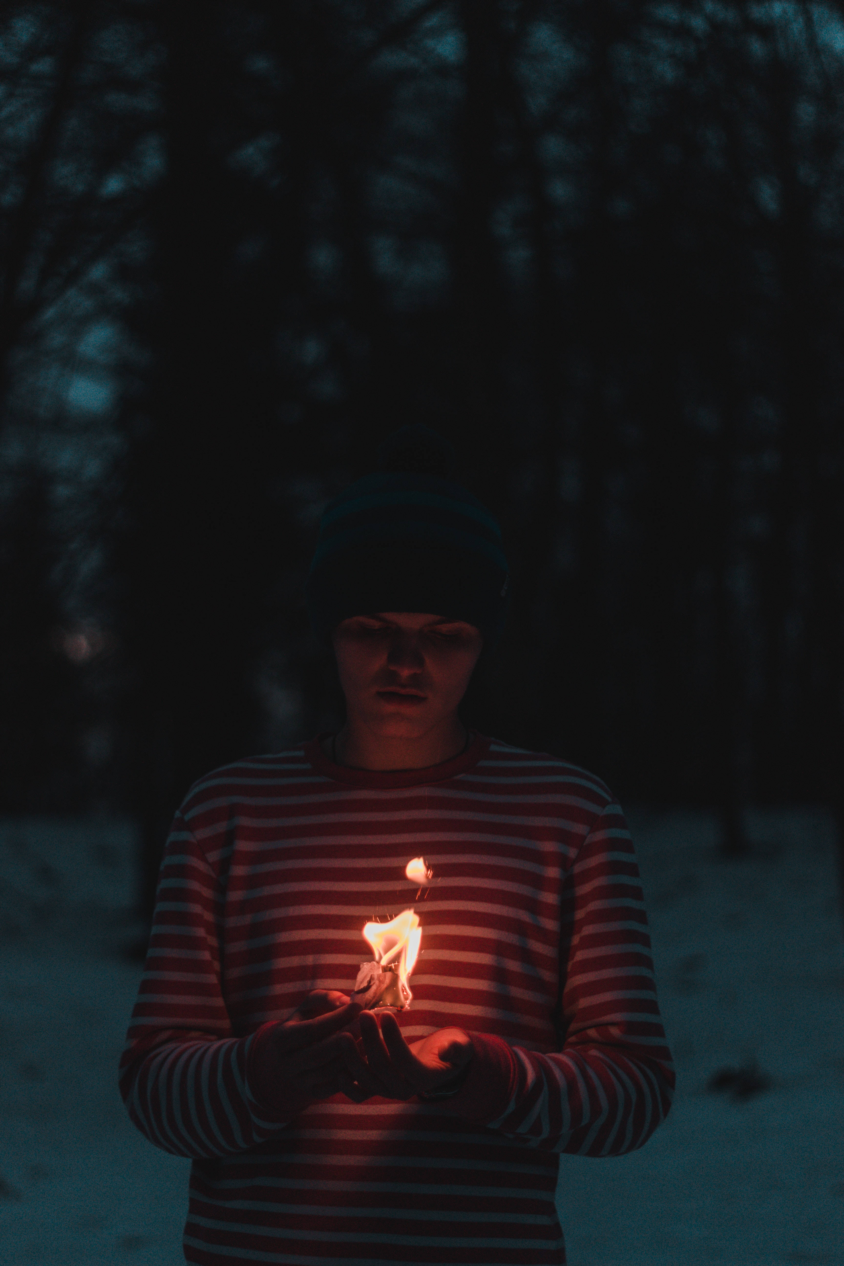 火焰動畫 桌布 壁紙 — 一個穿著條紋襯衫的人在雪夜森林中手持一支搖曳的蠟燭，溫暖的光線映照在他們的臉上。
