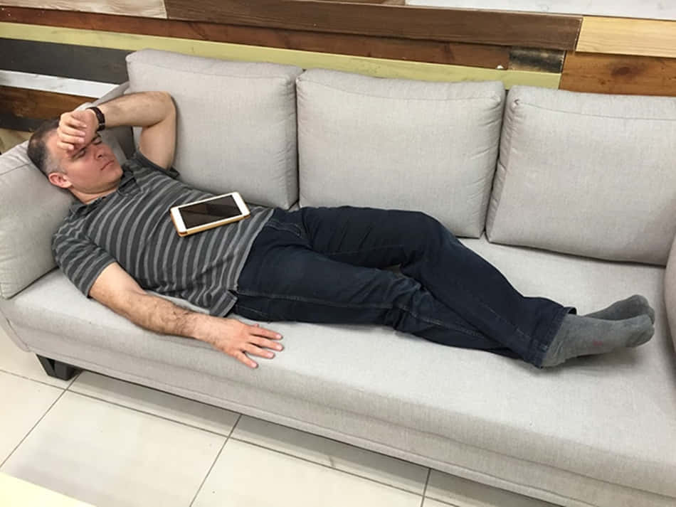 搞笑 桌布 壁紙 — 一個穿著條紋襯衫的男人筋疲力盡地躺在淺灰色沙發上，手機放在肚子上。