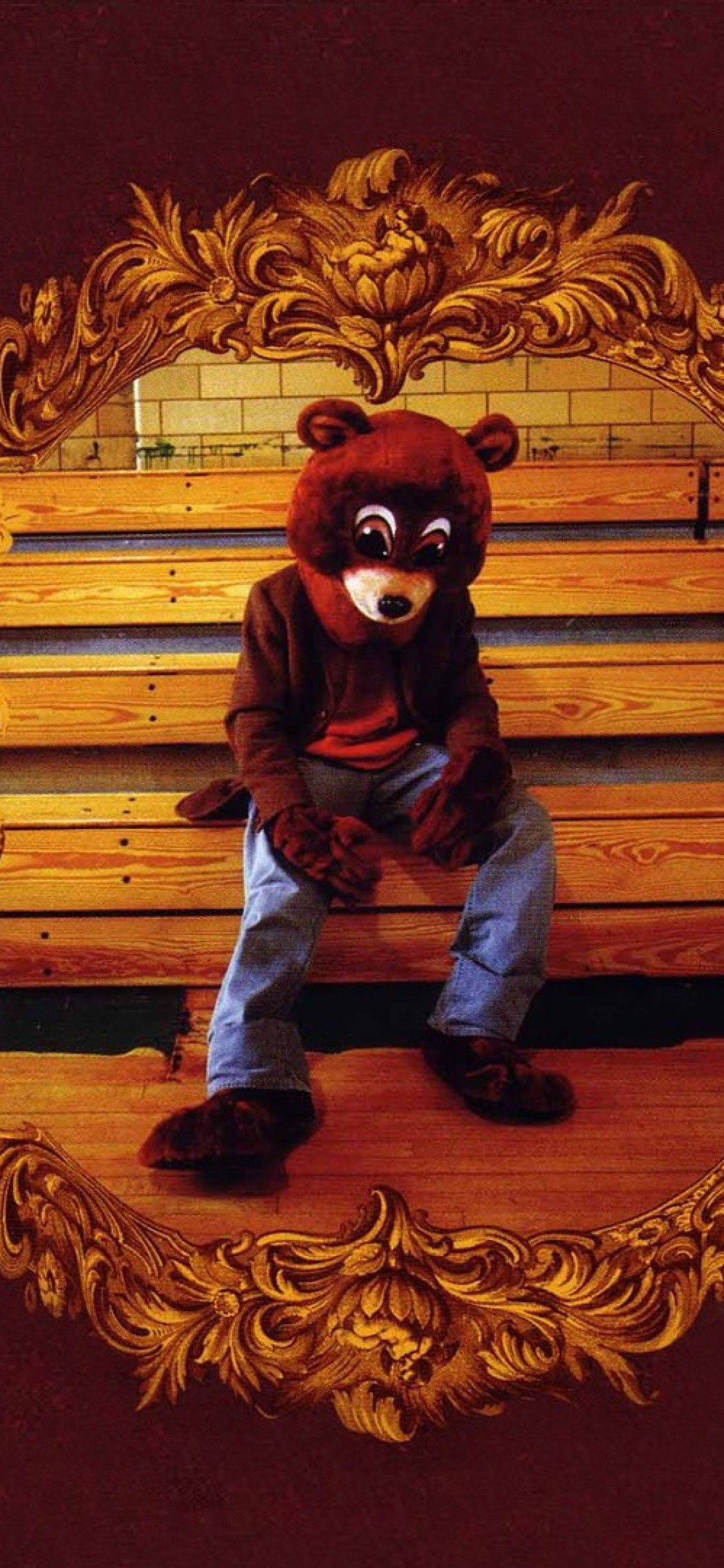 Kanye 桌布 壁紙 — 一個穿著棕色熊吉祥物服裝的人獨自坐在一張飾有金色雕刻的華麗木長椅上。