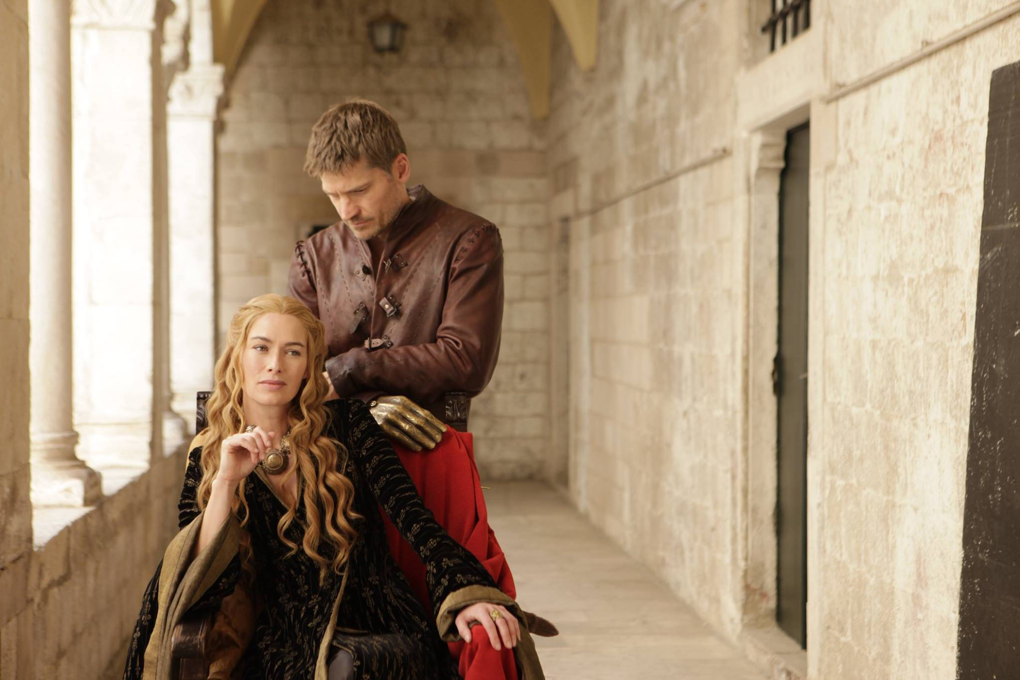cersei lannister 桌布 壁紙 — 一個穿著棕色皮革的男人站在一個穿著黑色和紅色長袍的坐著的女人後面，在石拱門下。