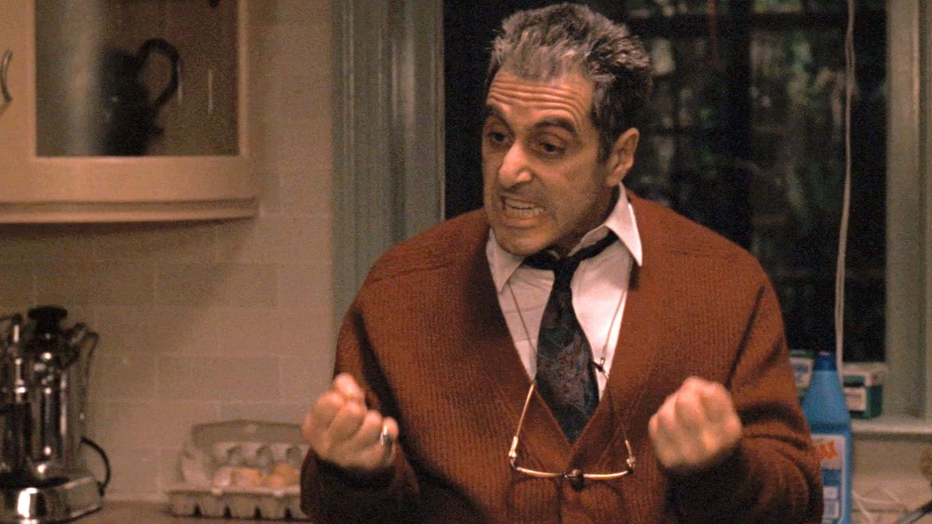 The Godfather 桌布 壁紙 — 一個穿著棕色開襟衫、領帶鬆開的男人，在身後有窗戶的廚房裡緊握拳頭。