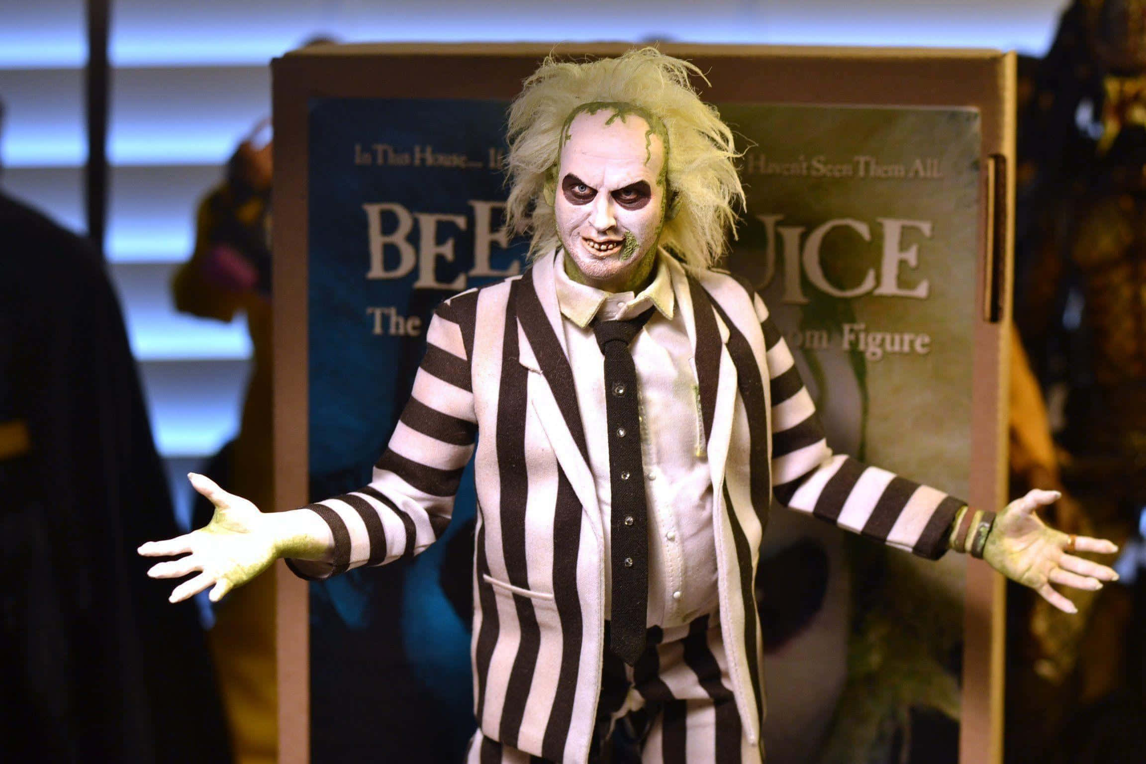 Beetlejuice 桌布 壁紙 — 一個穿著標誌性條紋西裝、頭髮狂野的Beetlejuice動作人偶，在電影海報背景下戲劇性地擺姿勢。