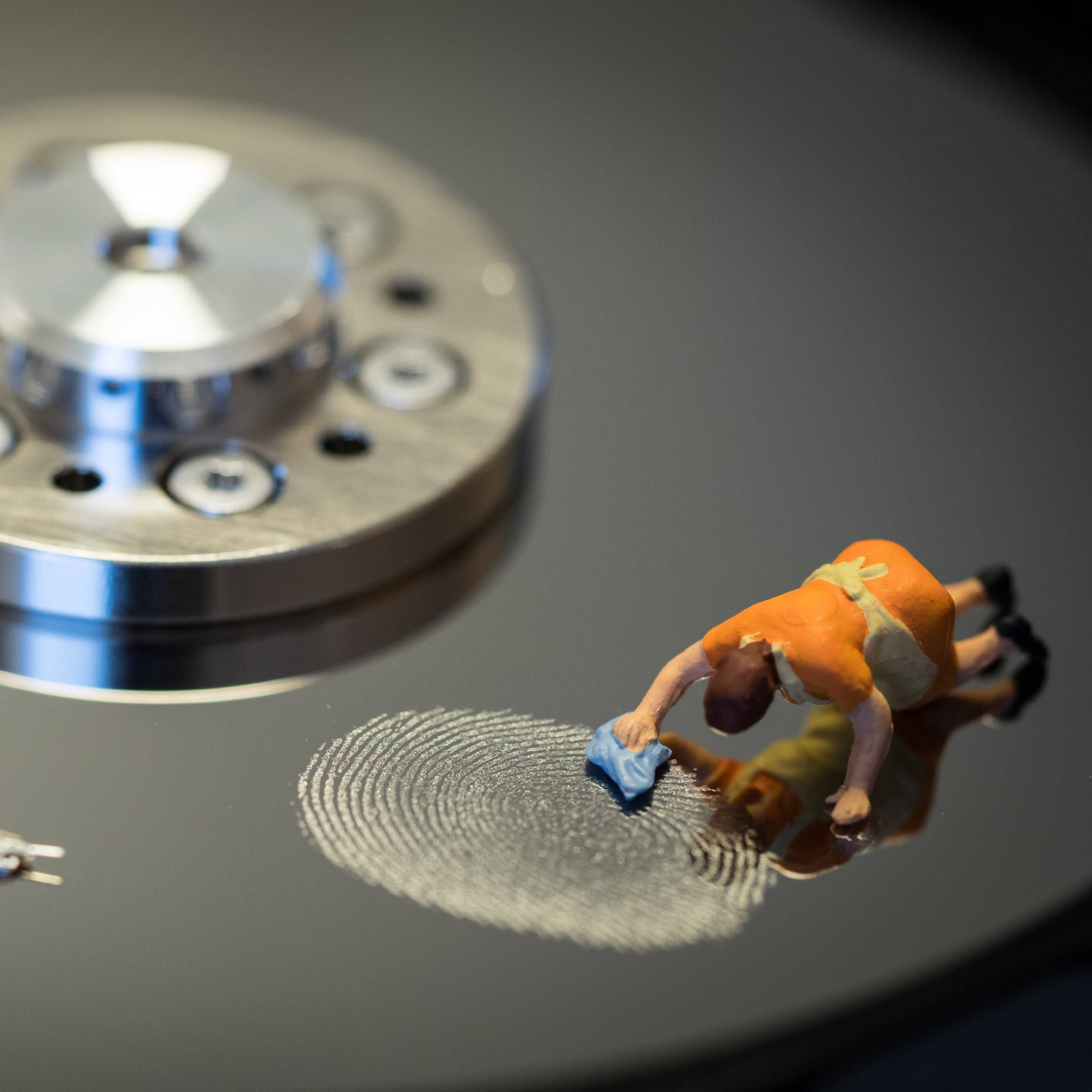 Hard Drive 桌布 壁紙 — 一個穿著橙色連身衣的小人偶正在仔細地擦拭硬碟碟片反射表面上的指紋。
