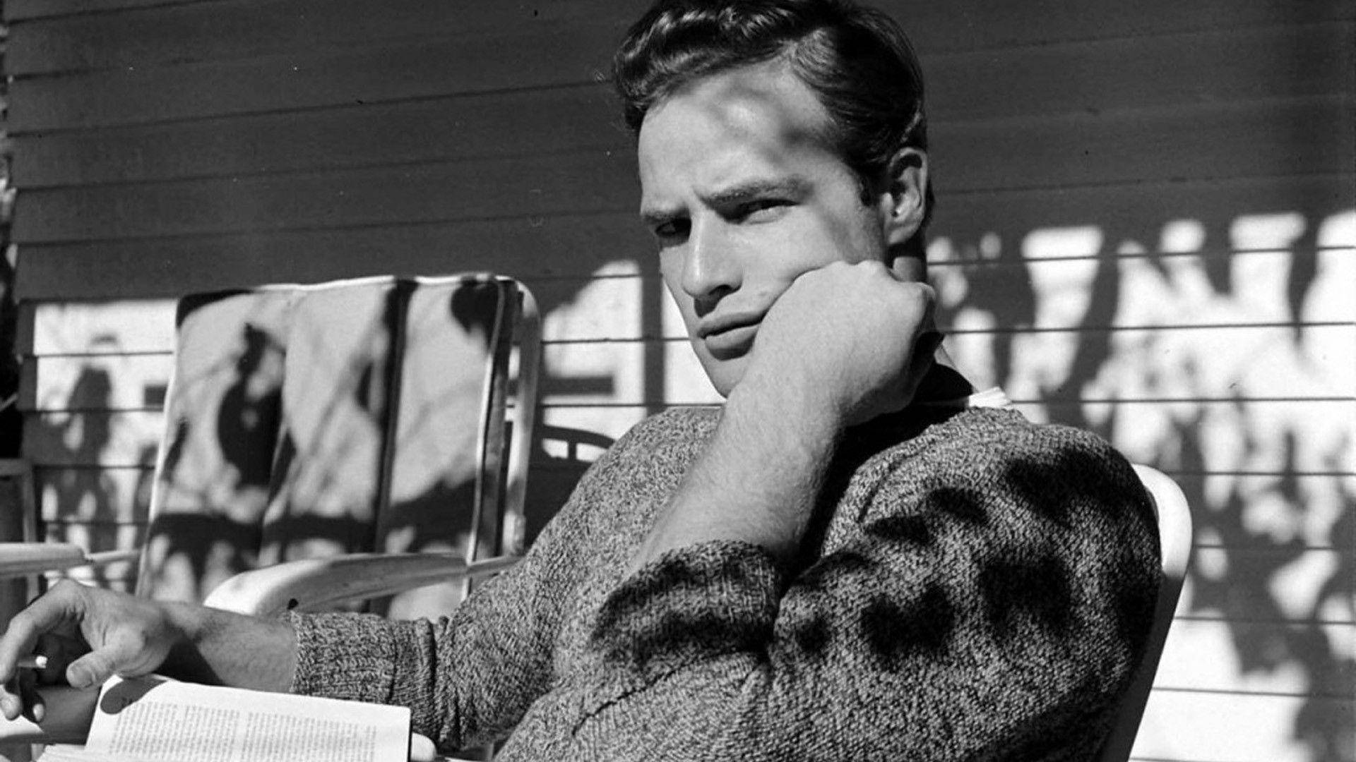 marlon brando 桌布 壁紙 — 一個穿著毛衣的男人在戶外用手托著下巴拿著書的黑白肖像。