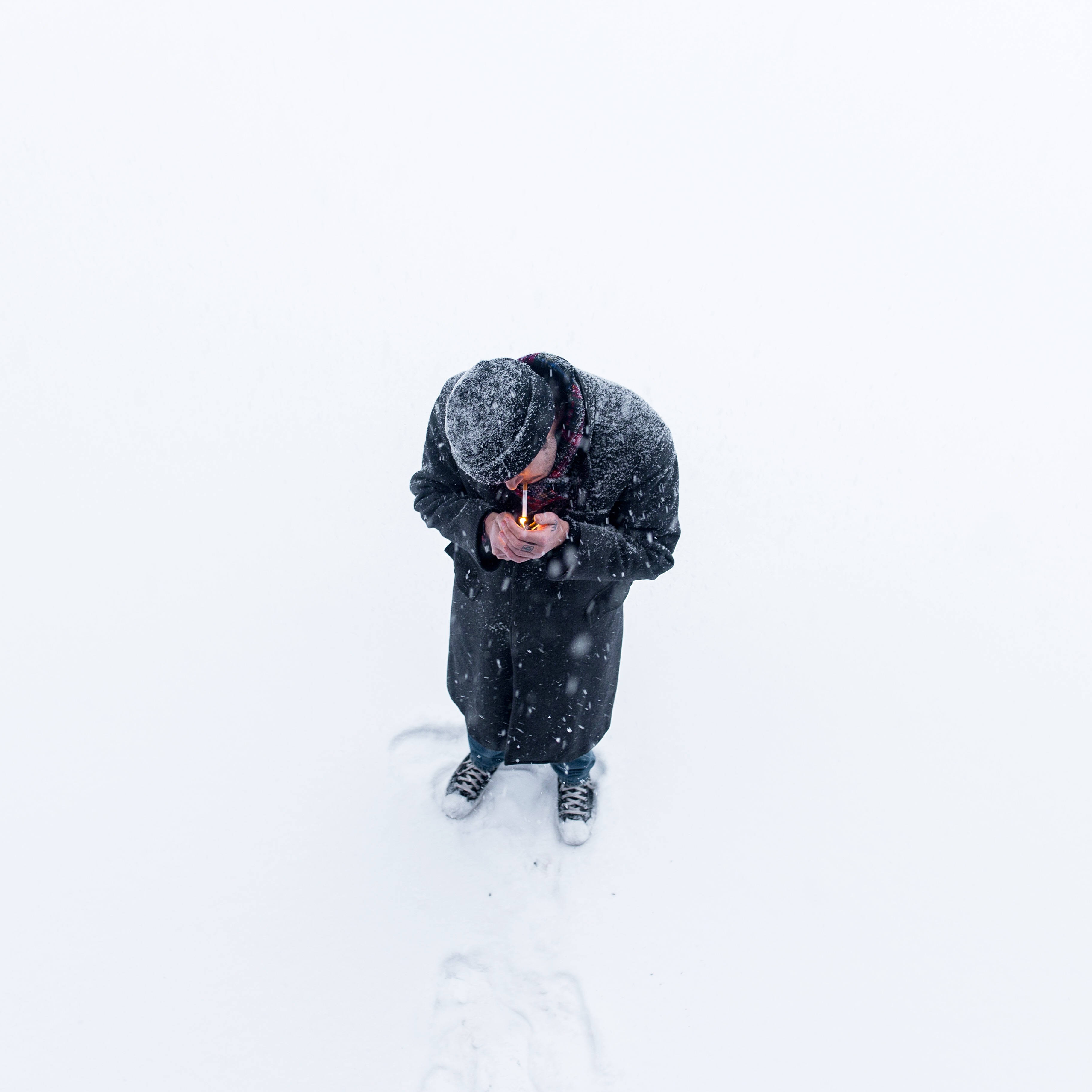 抽菸 桌布 壁紙 — 一個穿著深色冬季裝備的人獨自站在暴風雪中，手持點燃的蠟燭，面對白色的虛無。