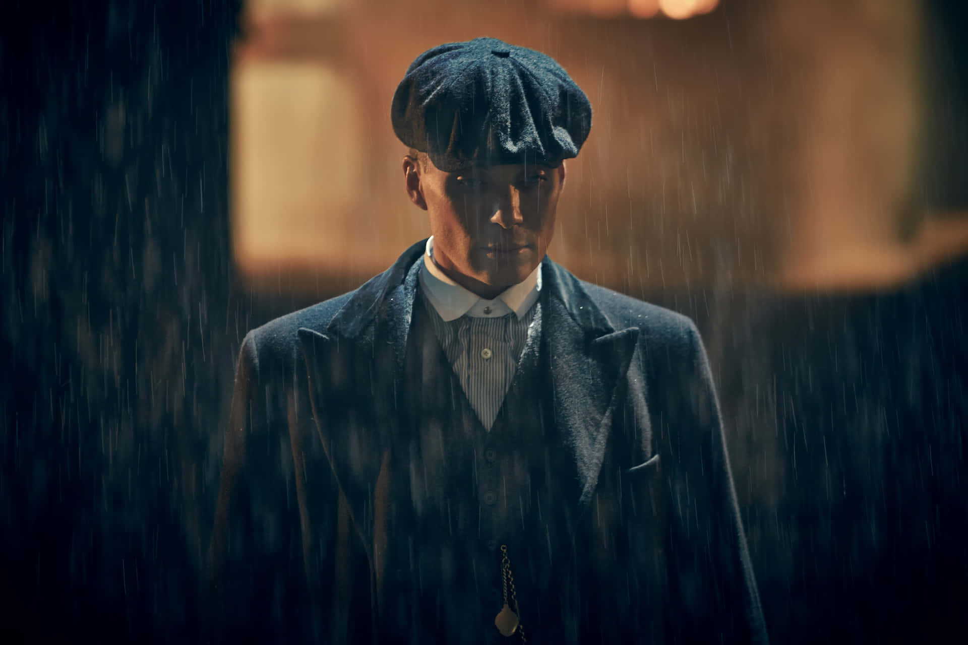 穿著時代外套和平頂帽的男人在戲劇性的燈光下站在雨中。 — Peaky Blinders 壁紙