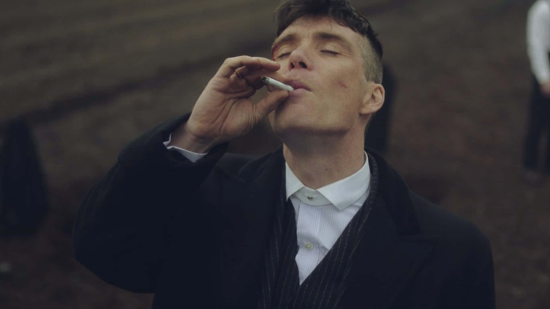 穿著深色外套的男人在戶外閉著眼睛抽煙。