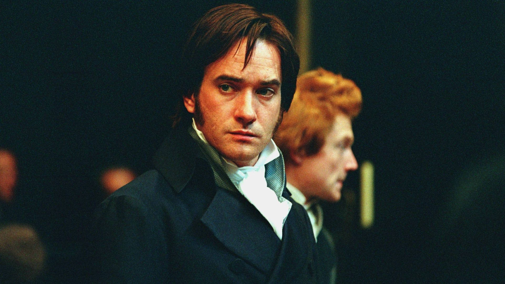 Pride And Prejudice 桌布 壁紙 — 一個穿著深色外套和白色領巾的男人在昏暗的房間裏專注地向前凝視，背景中另一個人模糊不清。