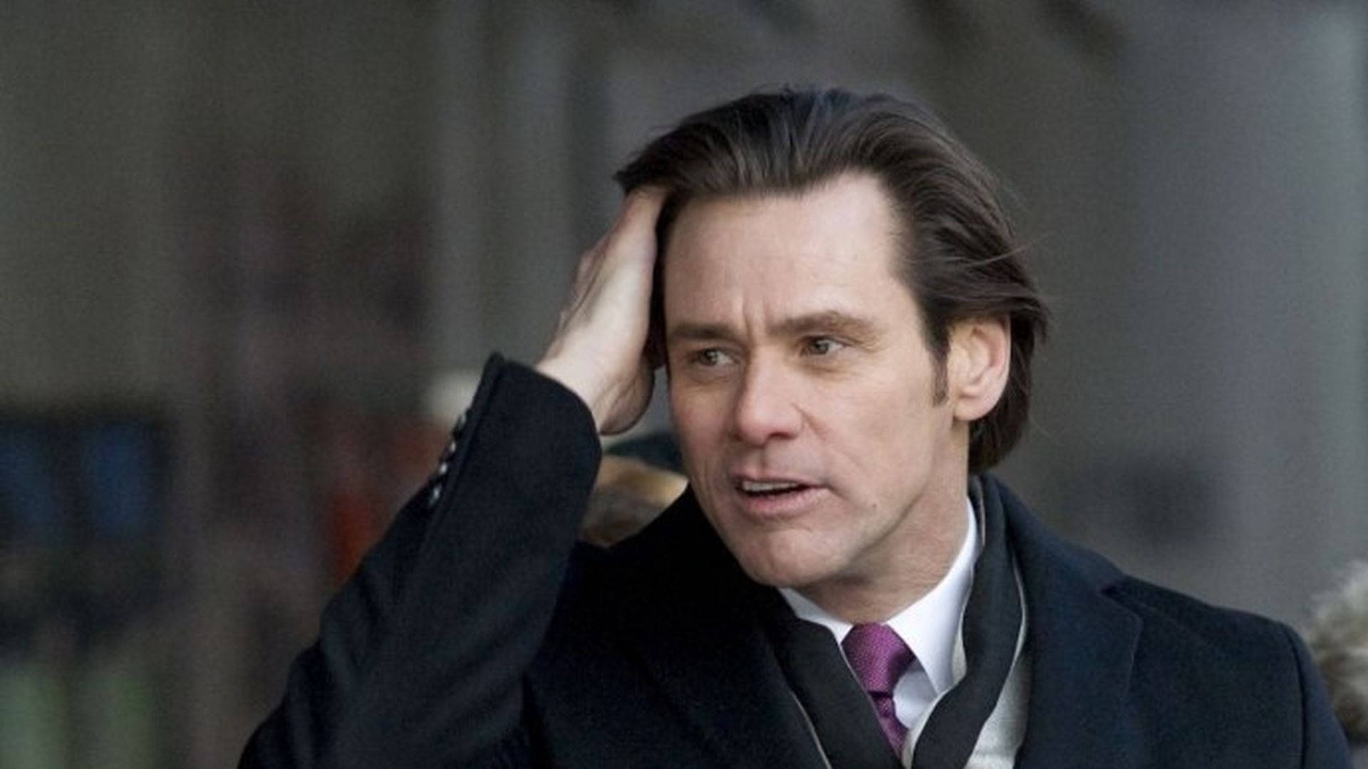 Jim Carrey 桌布 壁紙 — 一個穿著深色外套和紫色領帶的男人，在戶外用手撥頭髮，表情緊張。