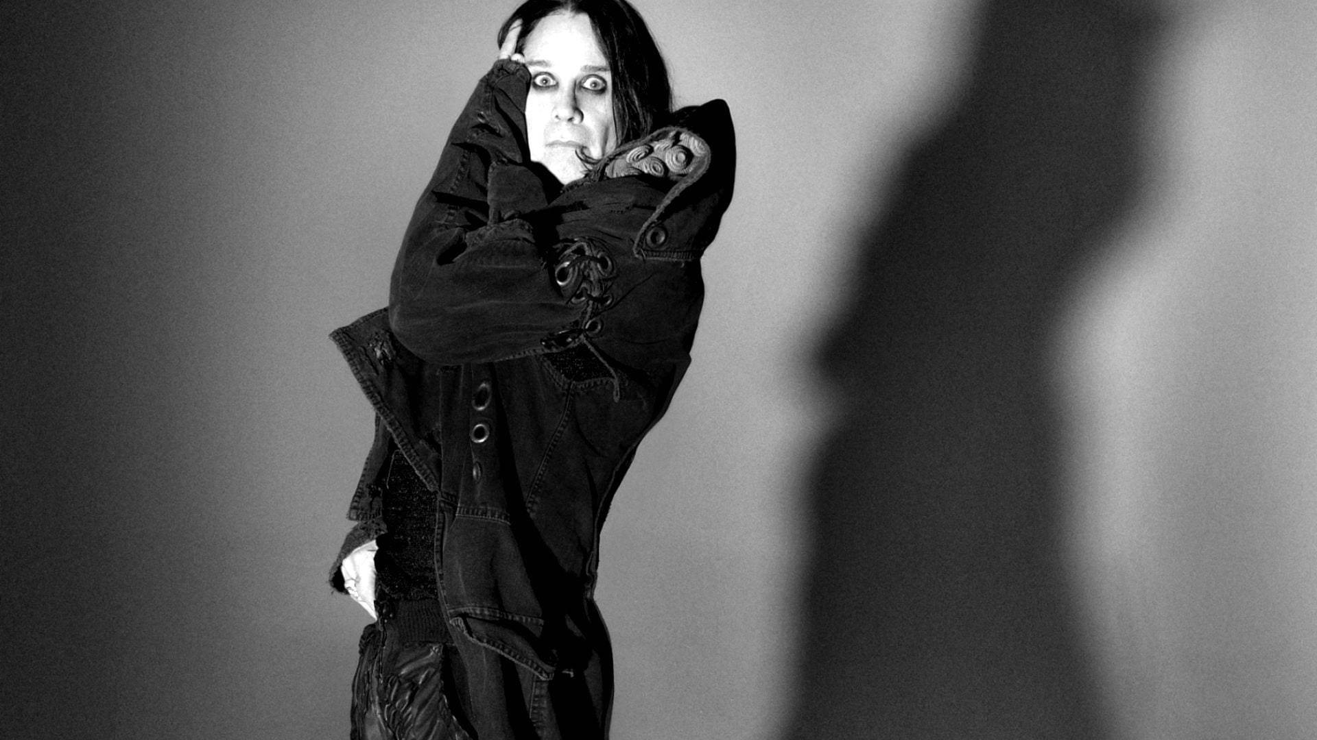 Ozzy Osbourne 桌布 壁紙 — 一個穿著深色外套的人站在素色牆前，旁邊投射出戲劇性的陰影，呈單色調。