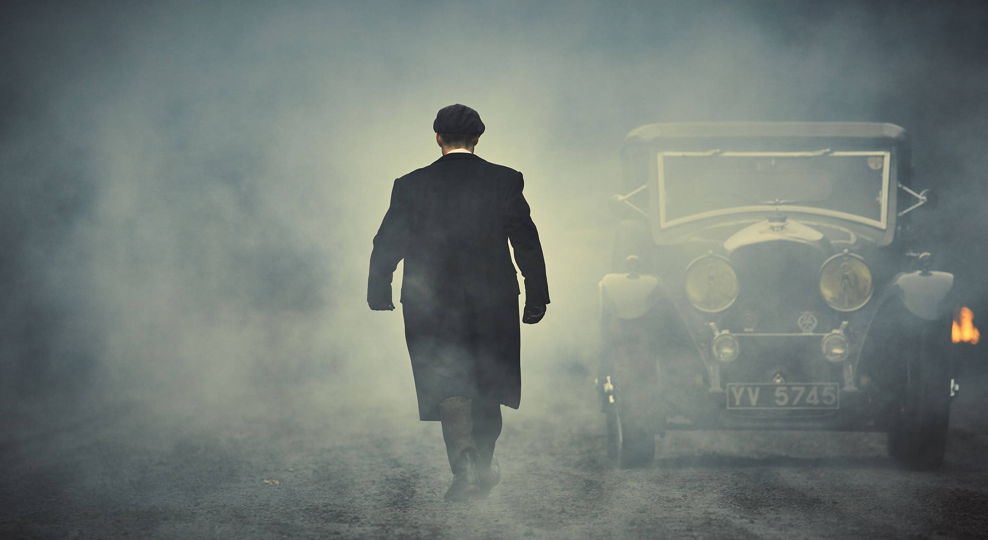 男人從燃燒的復古車旁走開，煙霧瀰漫 — Peaky Blinders 壁紙