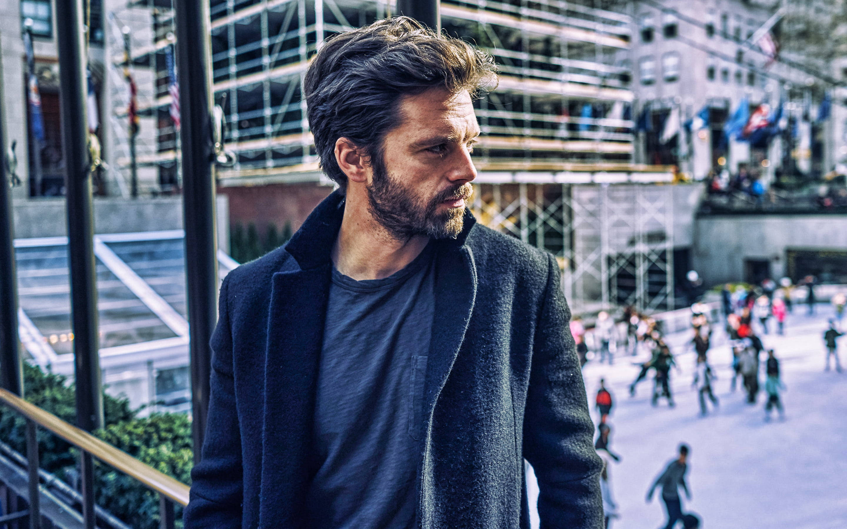 Sebastian 桌布 壁紙 — 一個穿著深色外套的男人站在城市陽台上，俯瞰下面熙熙攘攘的廣場和行人。
